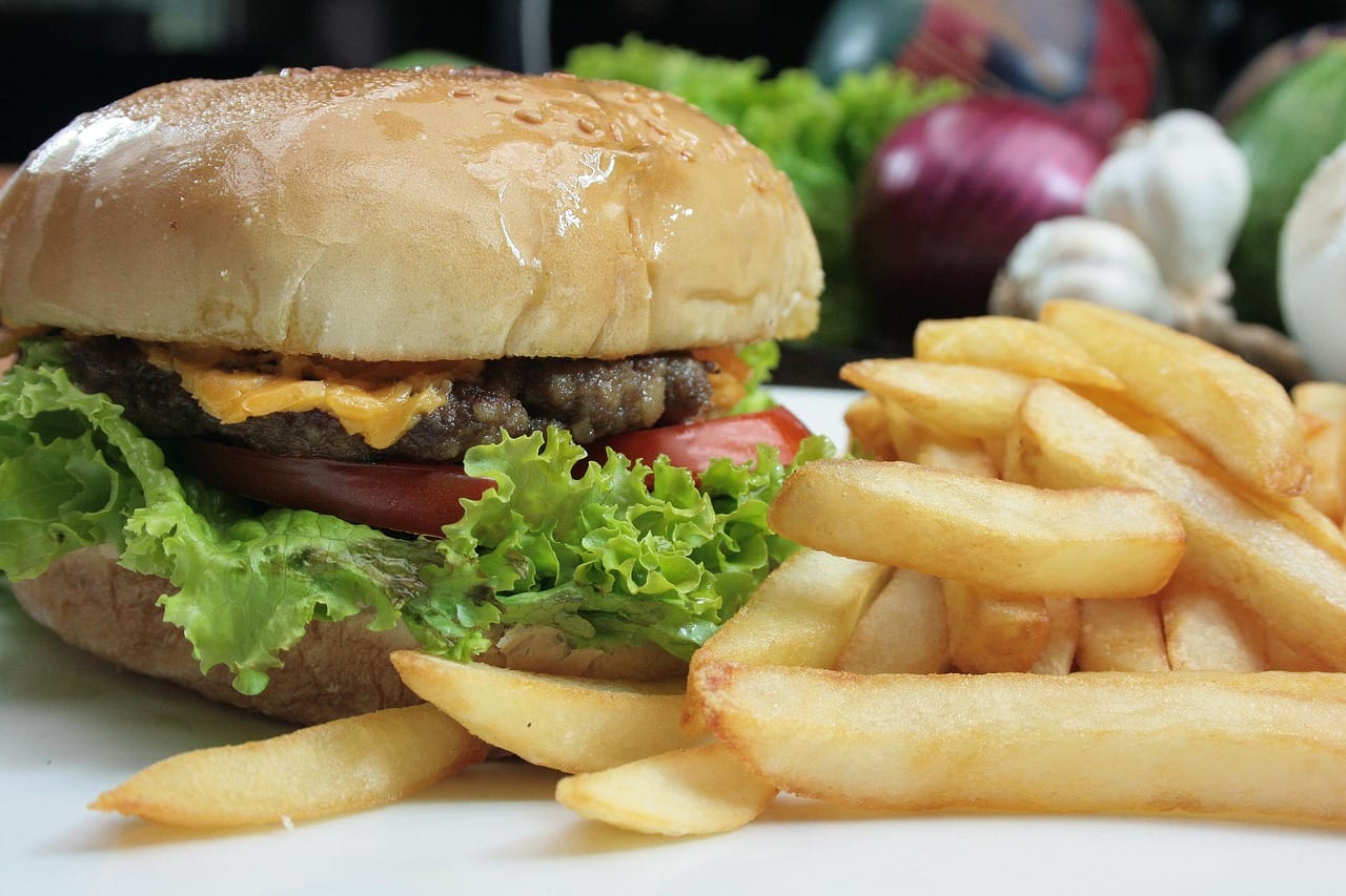 A person taking a large bite of a juicy cheeseburger at a table
