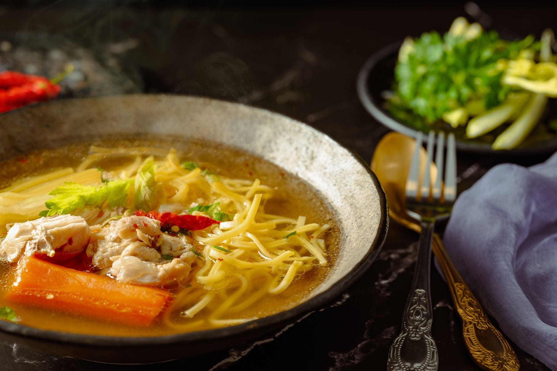 A steaming bowl of chicken soup with vegetables on a wooden table