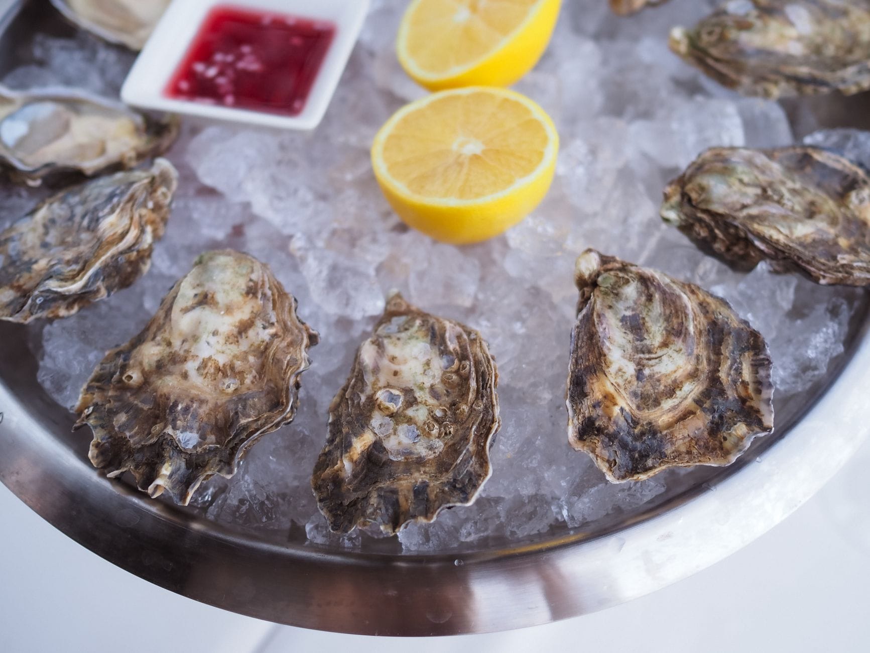 A platter of freshly shucked oysters on crushed ice with lemon wedges