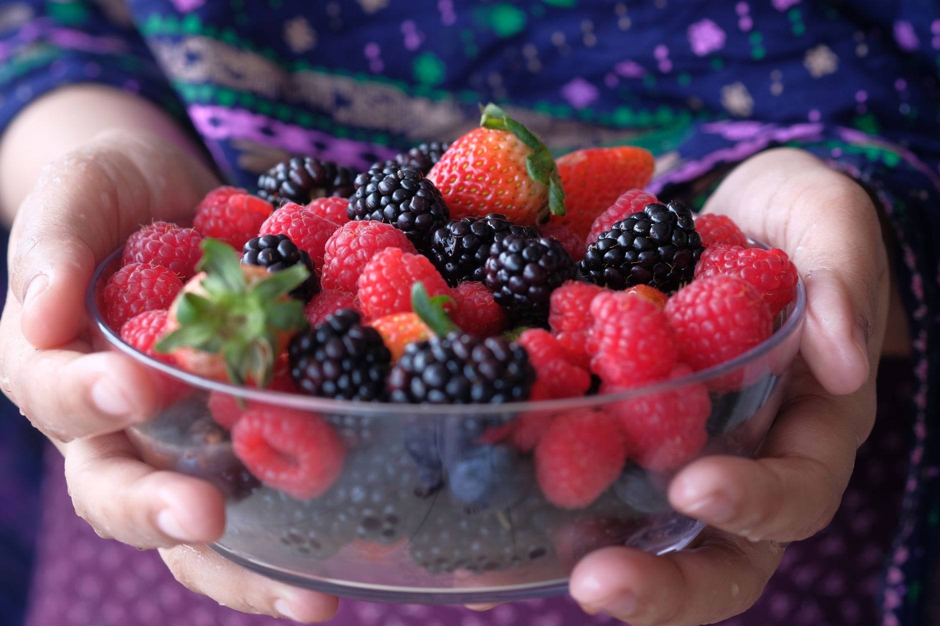 A white bowl filled with blueberries strawberries and raspberries on wood