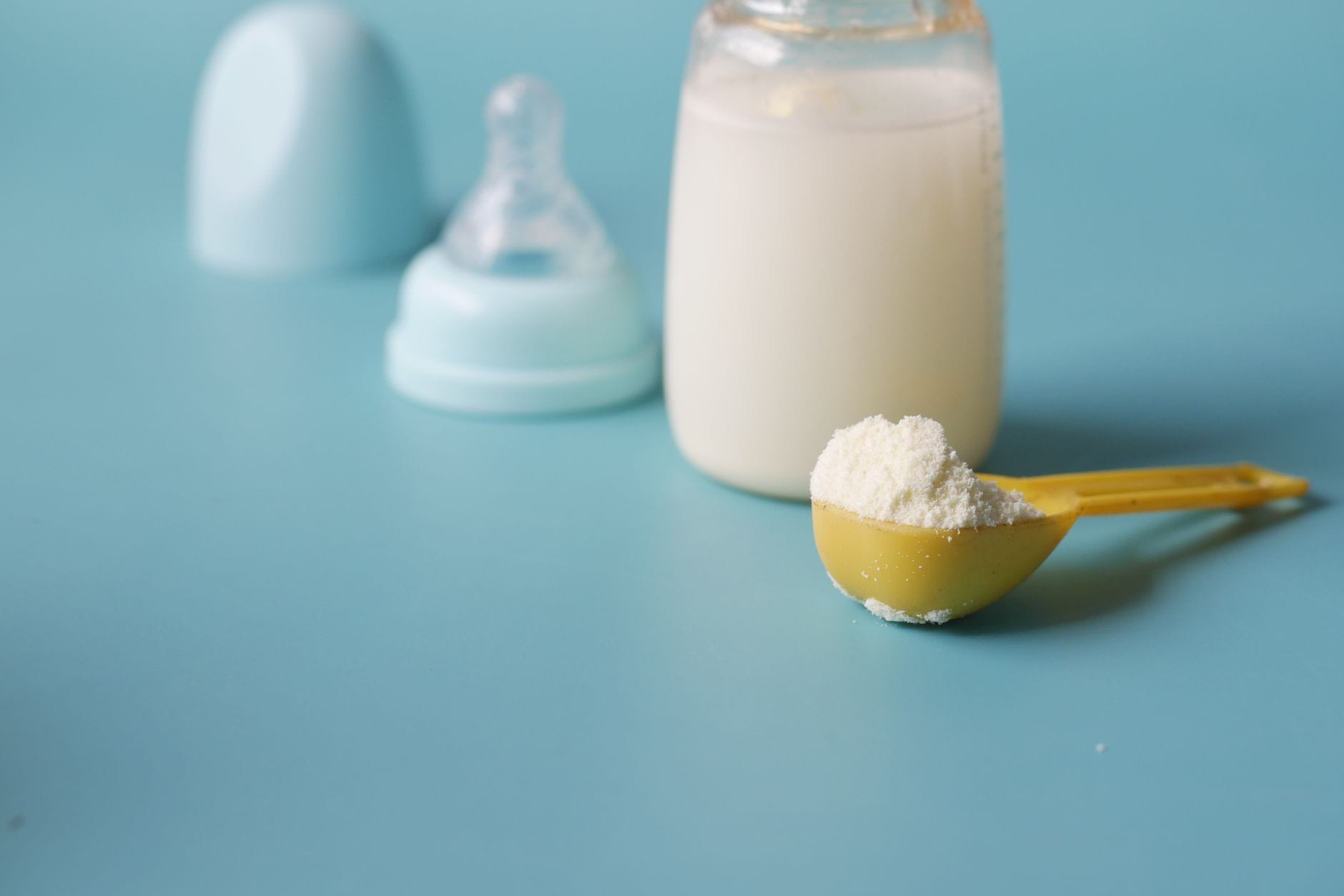 A measuring scoop filled with beige nutritional powder above an open tub