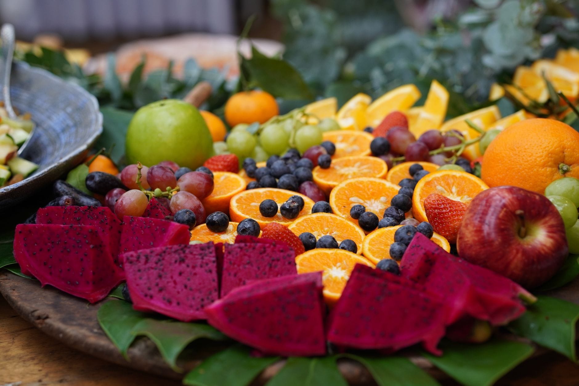 A wooden bowl piled with apples, bananas, and other whole fruit on a kitchen counter