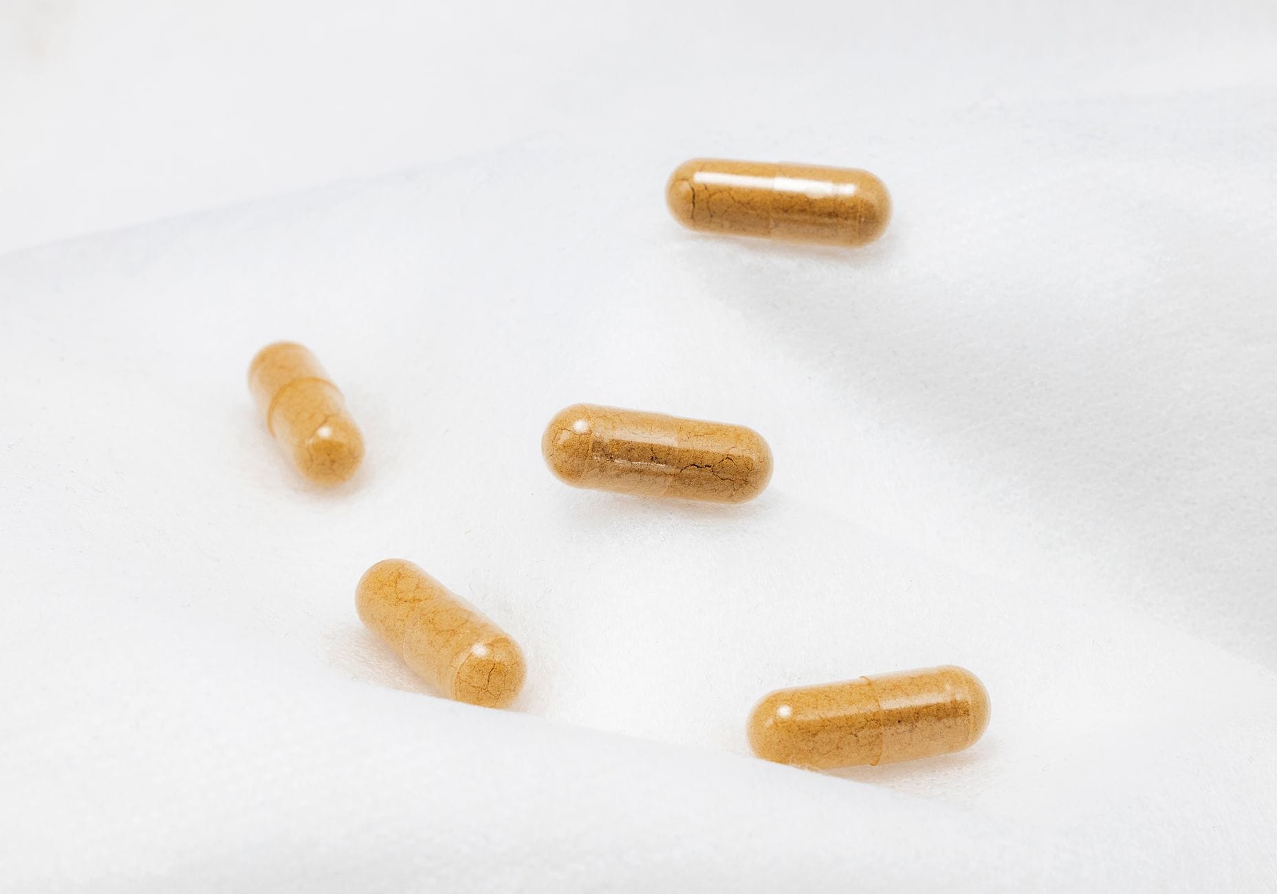 Amber herbal capsules spilling from a bottle onto a wooden table