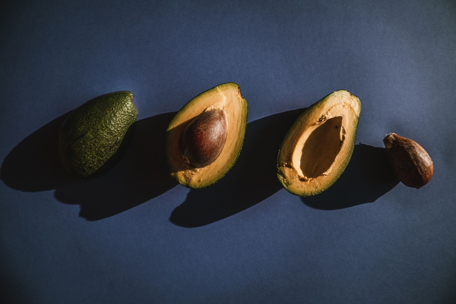 A halved avocado showing green flesh and a large brown pit