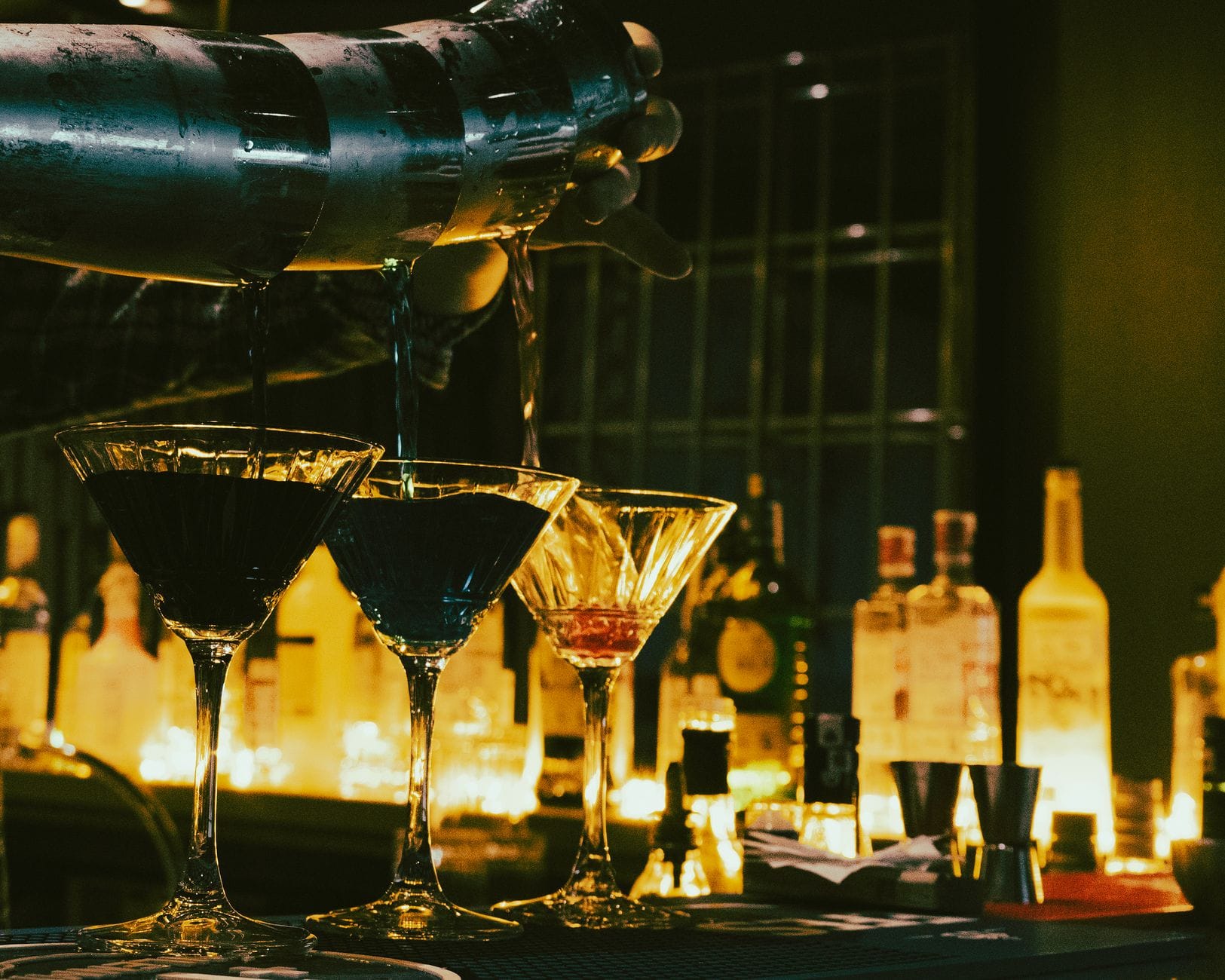A bartender pouring a clear cocktail into a coupe glass with fresh garnish