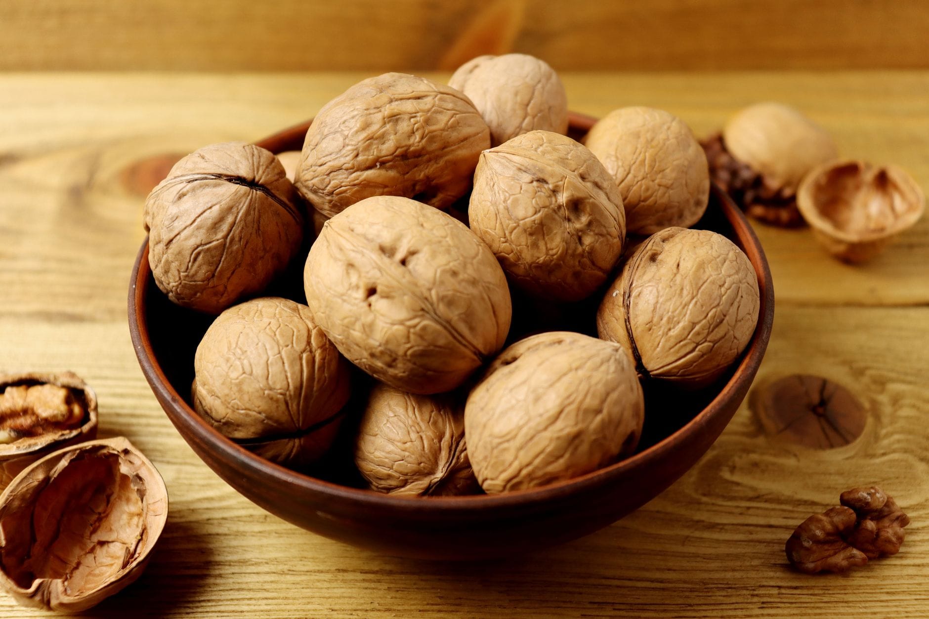 Whole walnuts spilling from a small wooden bowl onto rustic wood