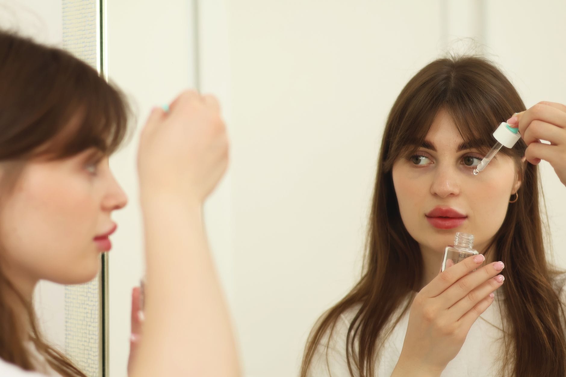 Woman smiling as she applies moisturizer to her face in a mirror