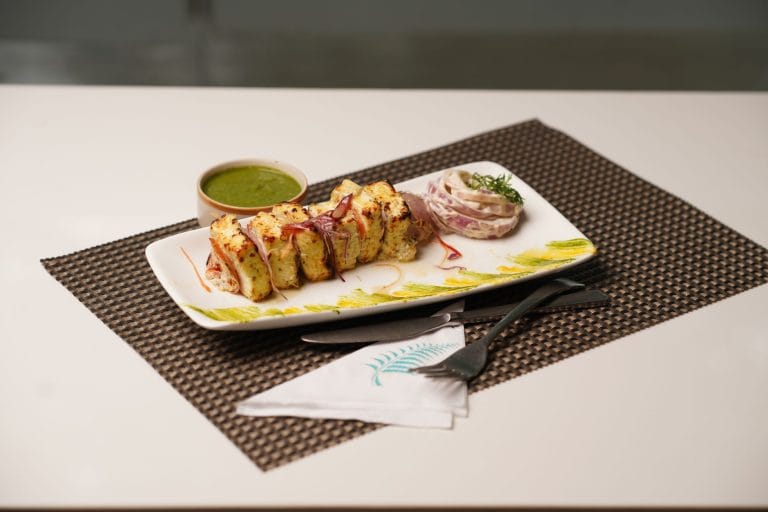 Cubes of fresh white paneer stacked on a dark plate with herbs