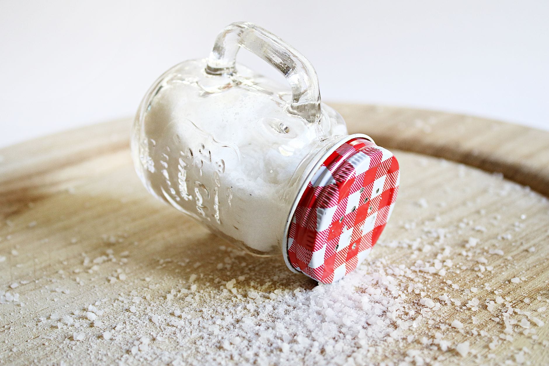 white salt crystals pouring from a glass shaker onto a dark surface