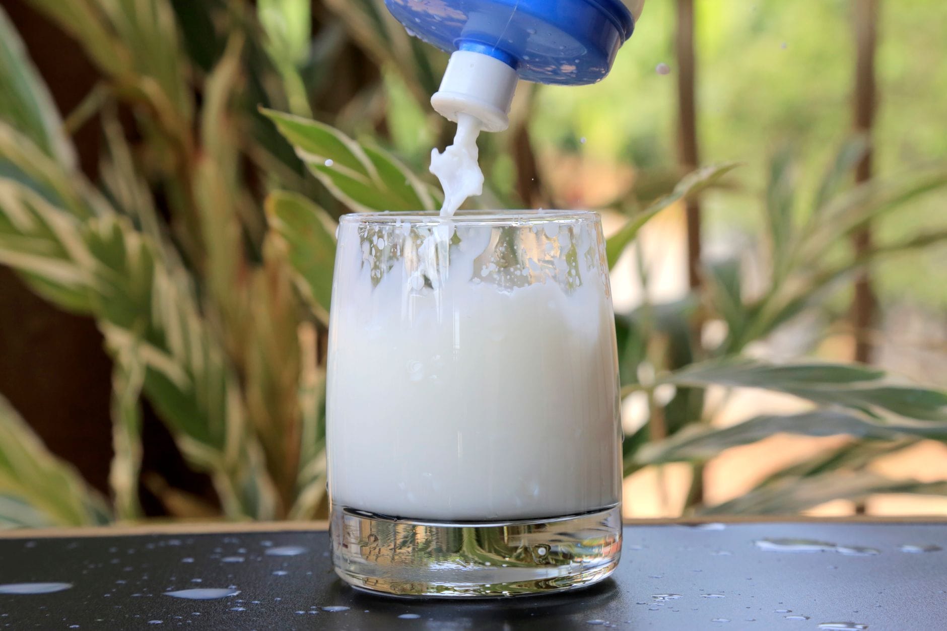 A hand pouring white milk into a clear glass on a counter