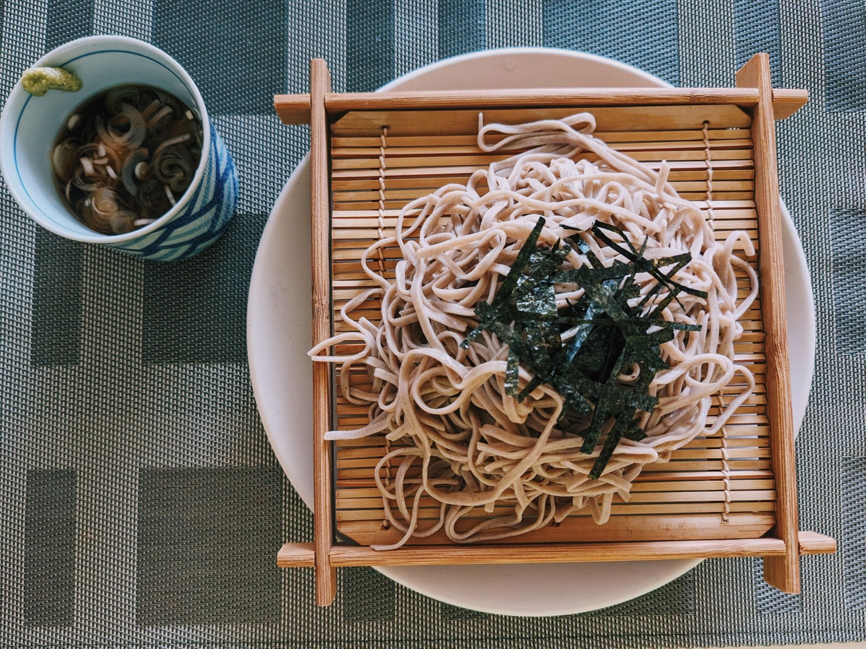 Cold buckwheat noodles arranged on a woven bamboo tray with dipping sauce