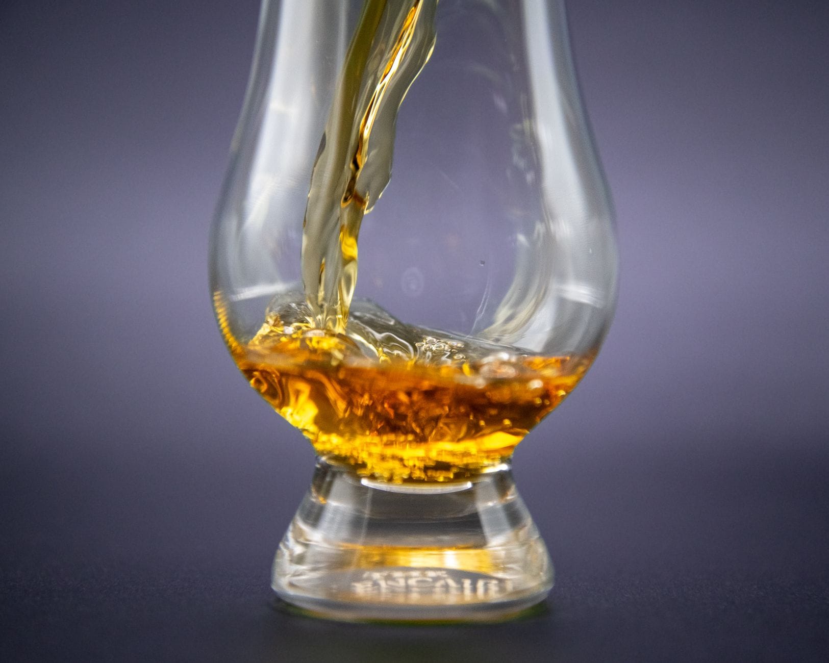 Amber whiskey being poured into a short crystal tumbler on a dark bar