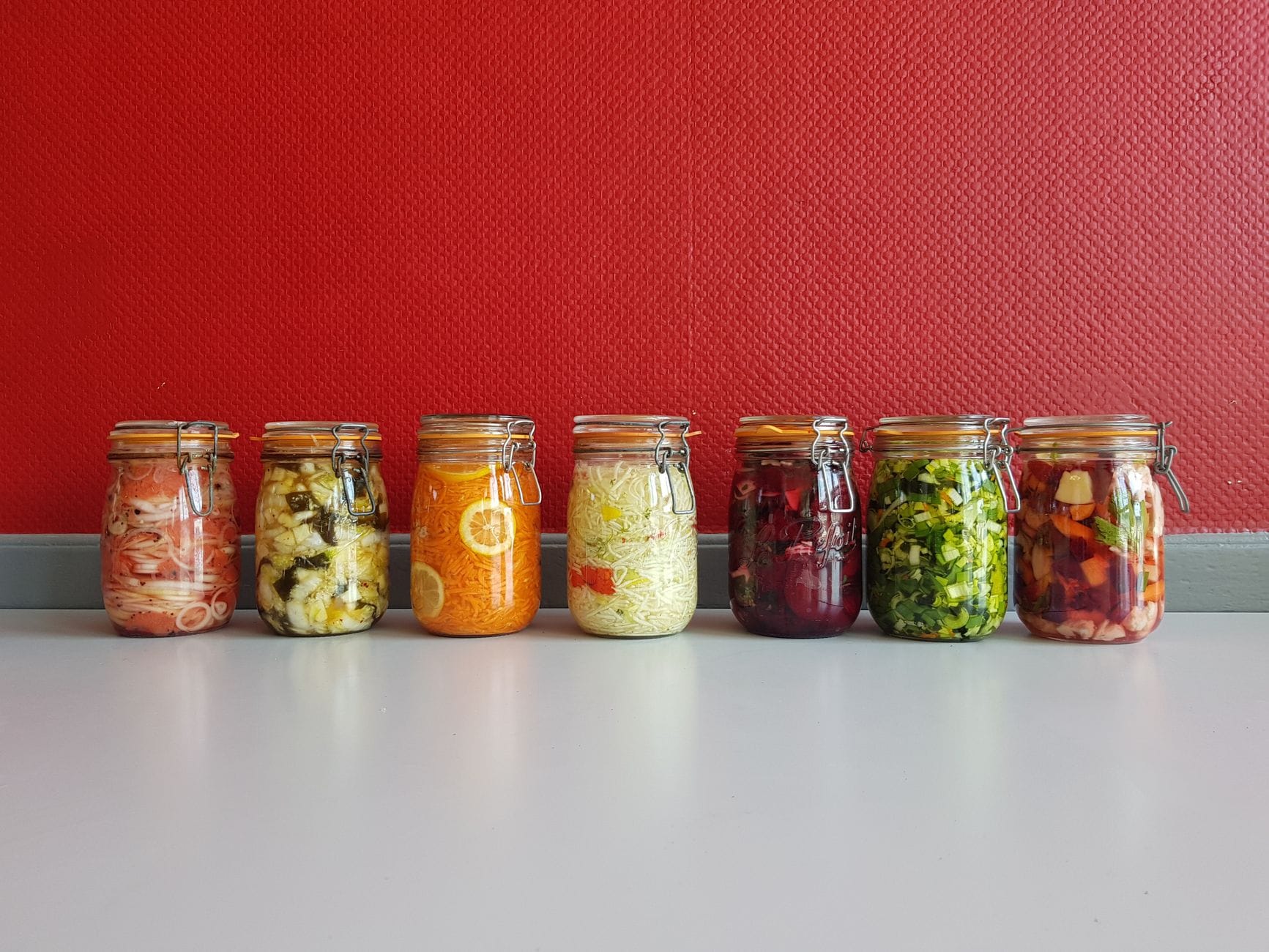 Glass jars of colorful fermented vegetables lined up on a wooden counter