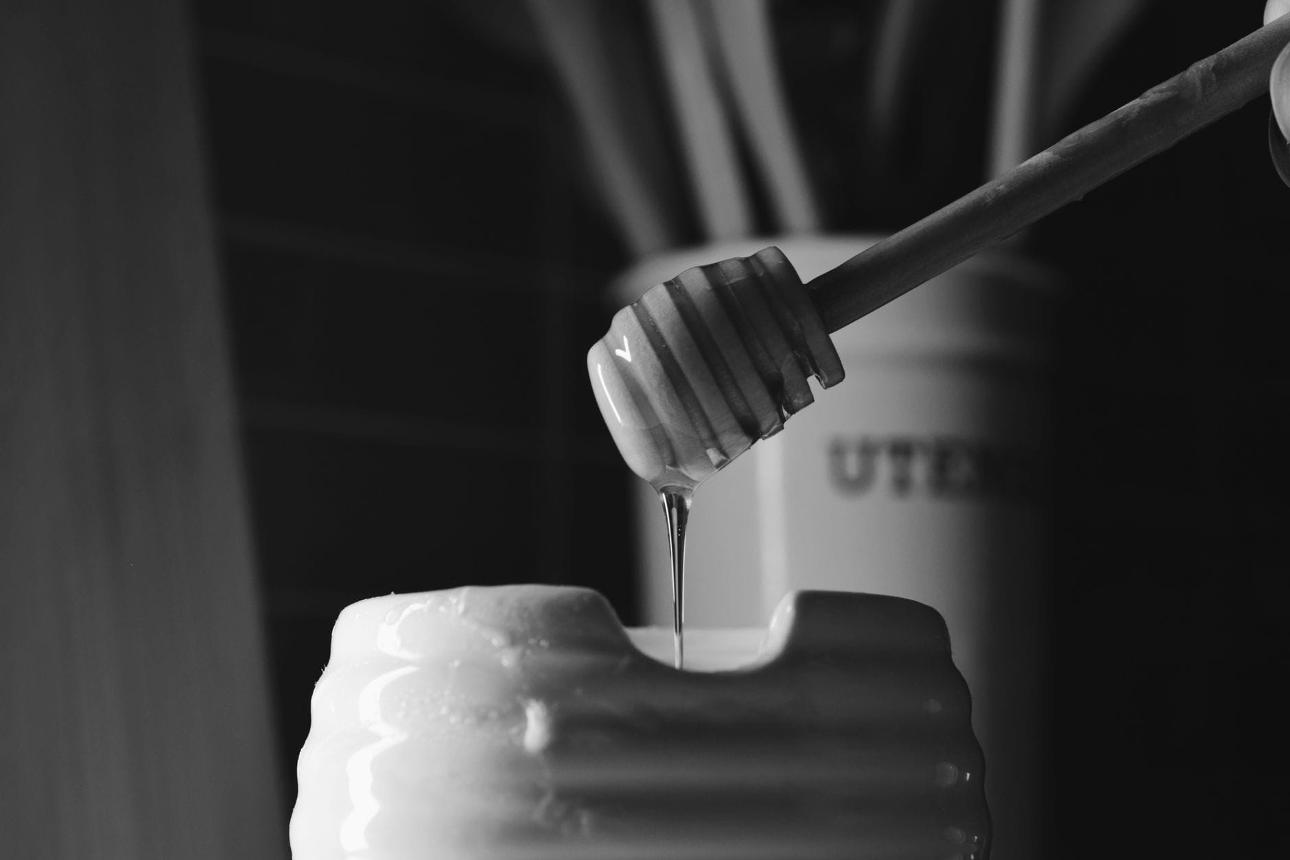 Wooden honey dipper resting across an open jar of golden honey