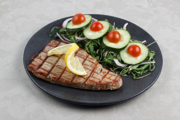 Seared tuna steak on a plate with lemon wedges and fresh herbs