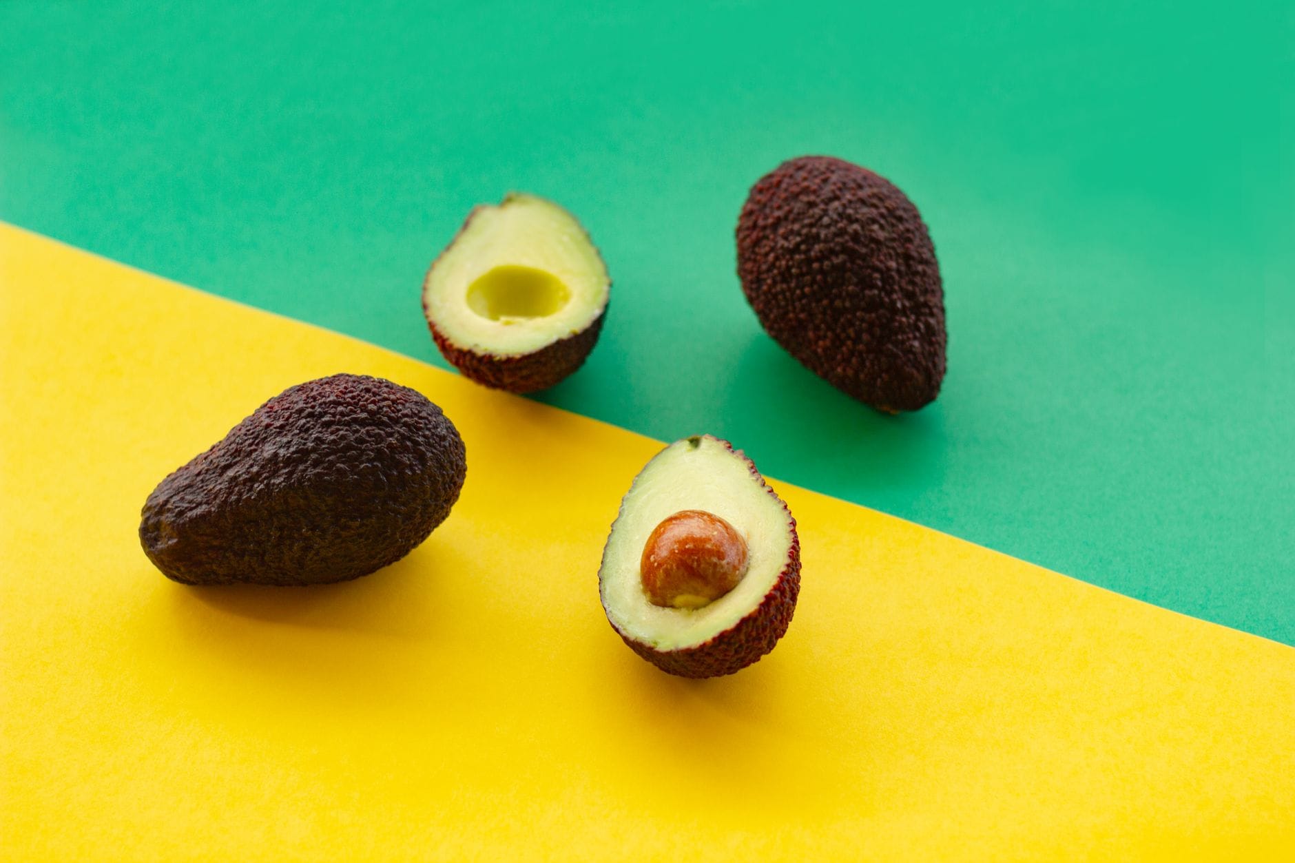 Two avocado halves on a wooden board beside scattered almonds