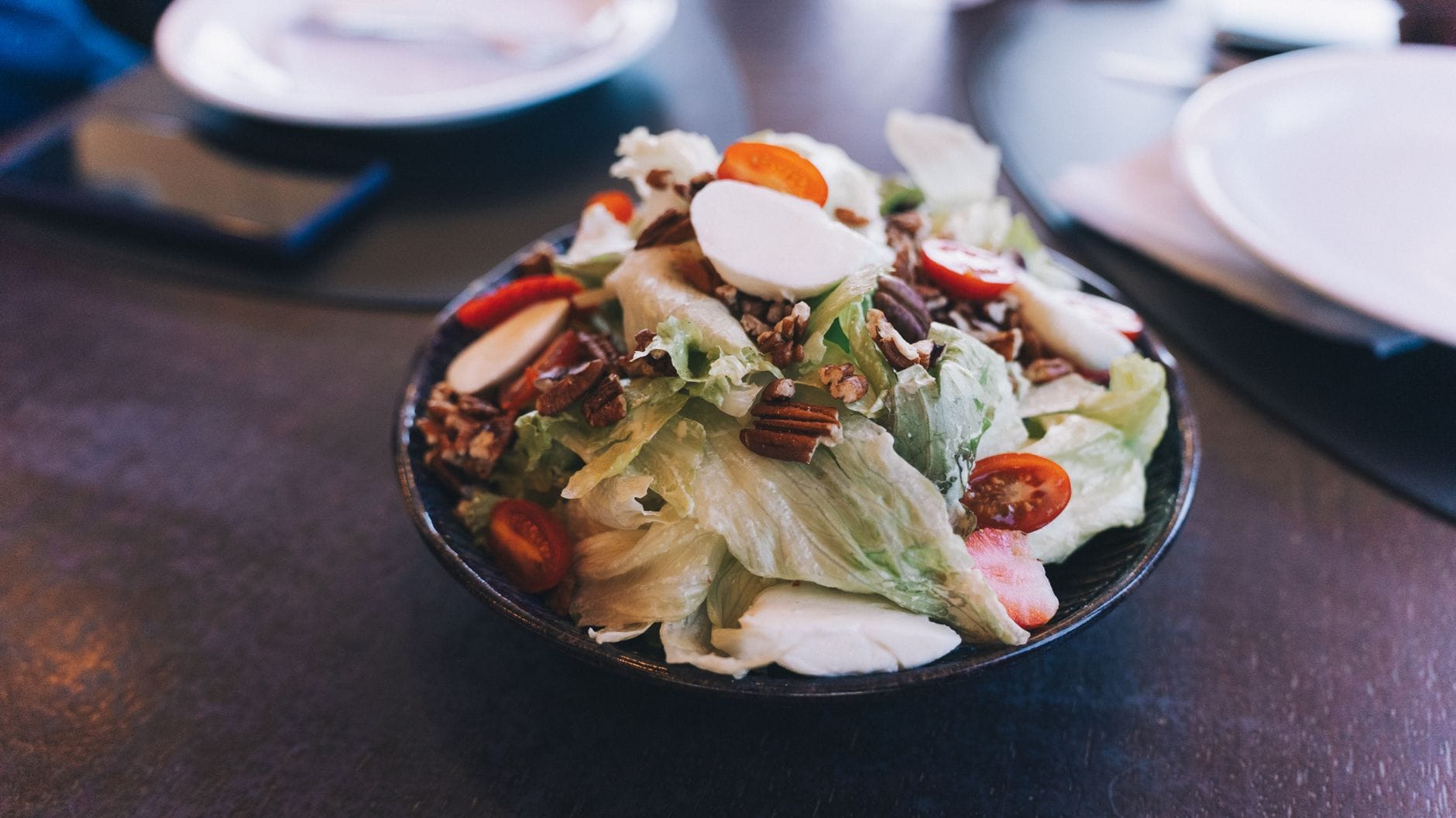 A wooden bowl of mixed greens and chopped vegetables on a table