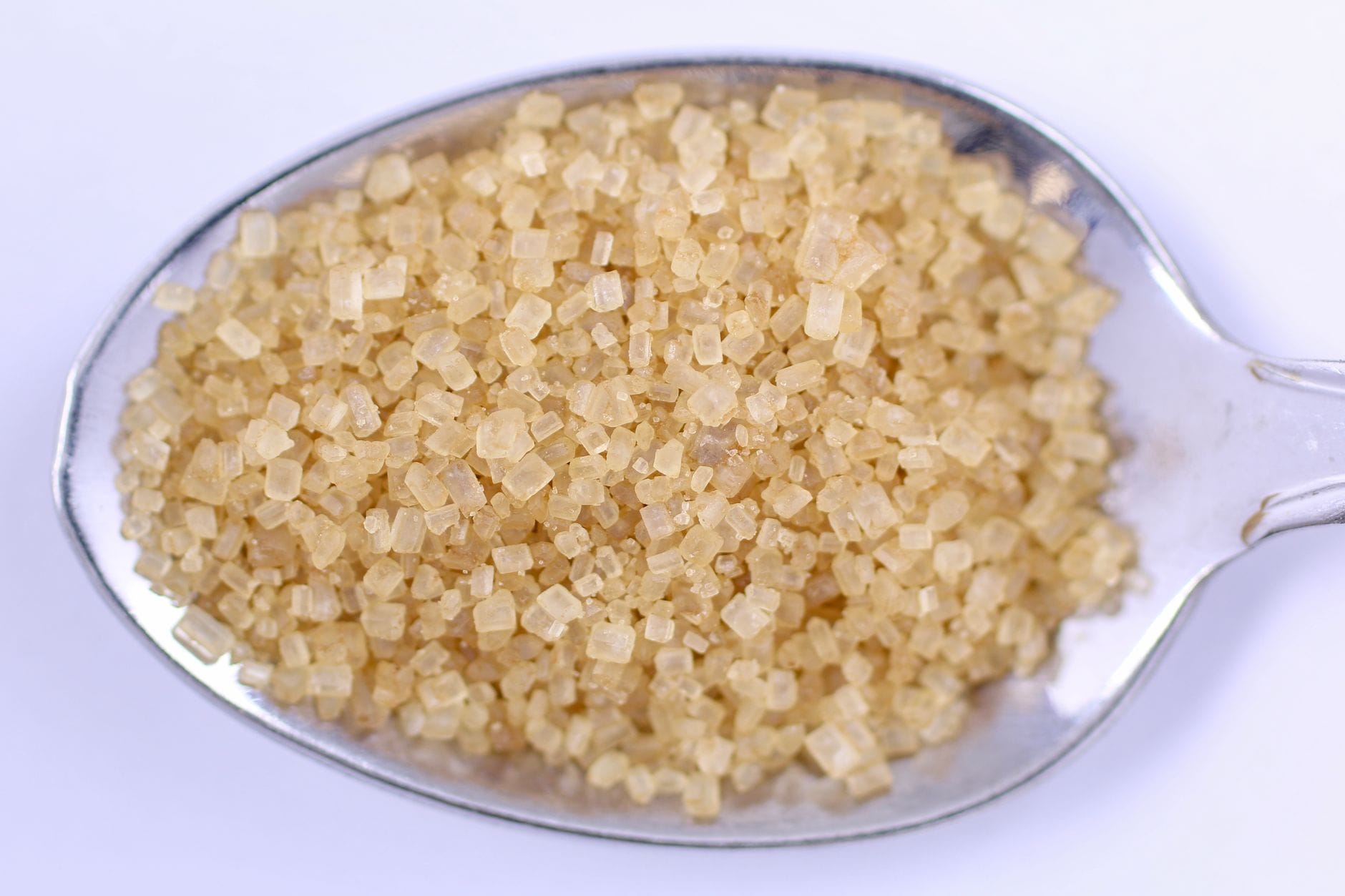 A wooden spoon heaped with soft brown sugar resting on a dark surface