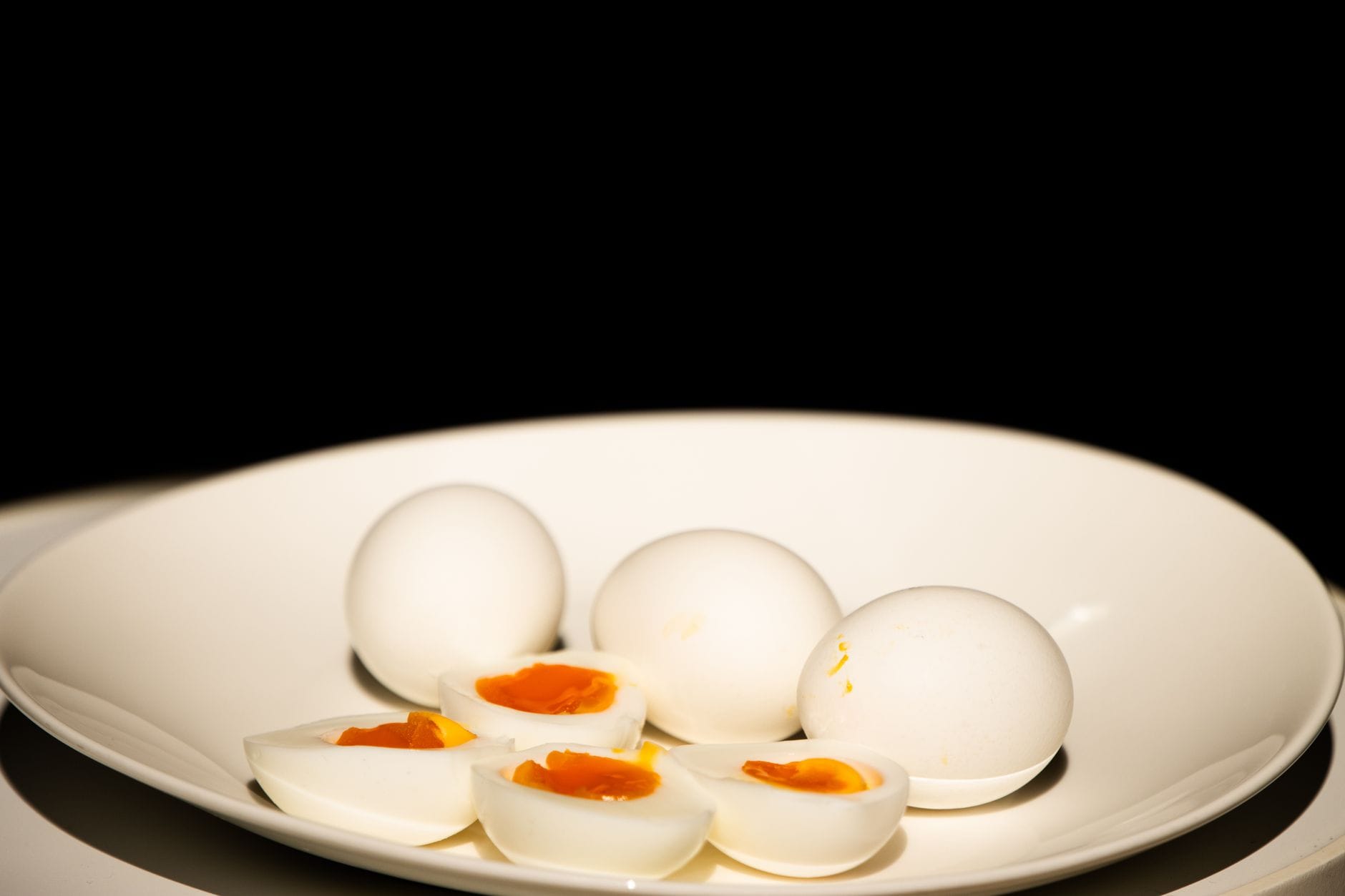 Two halved hard-boiled eggs beside sliced tomato on a small plate