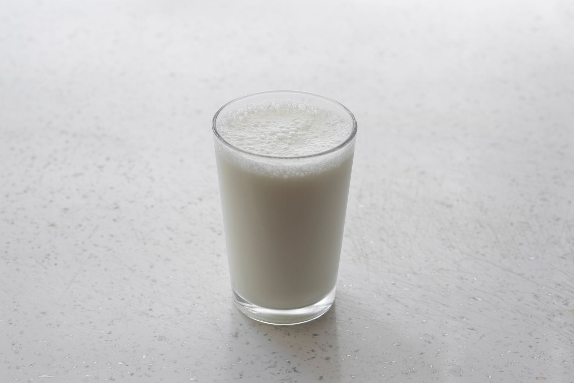 A tall glass of milk poured beside scattered almonds on wood