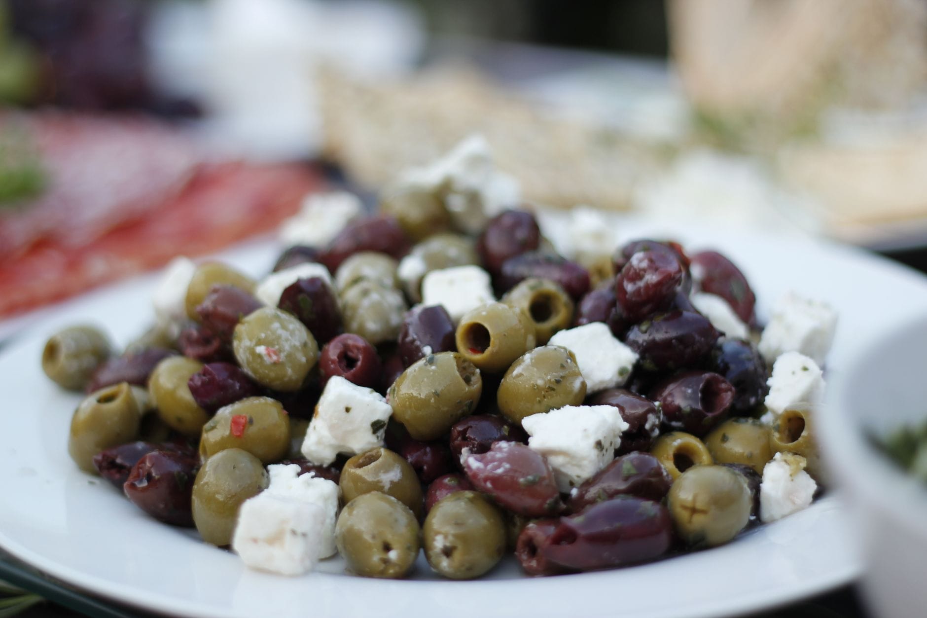 White feta cubes beside black olives and cucumber slices on a ceramic dish