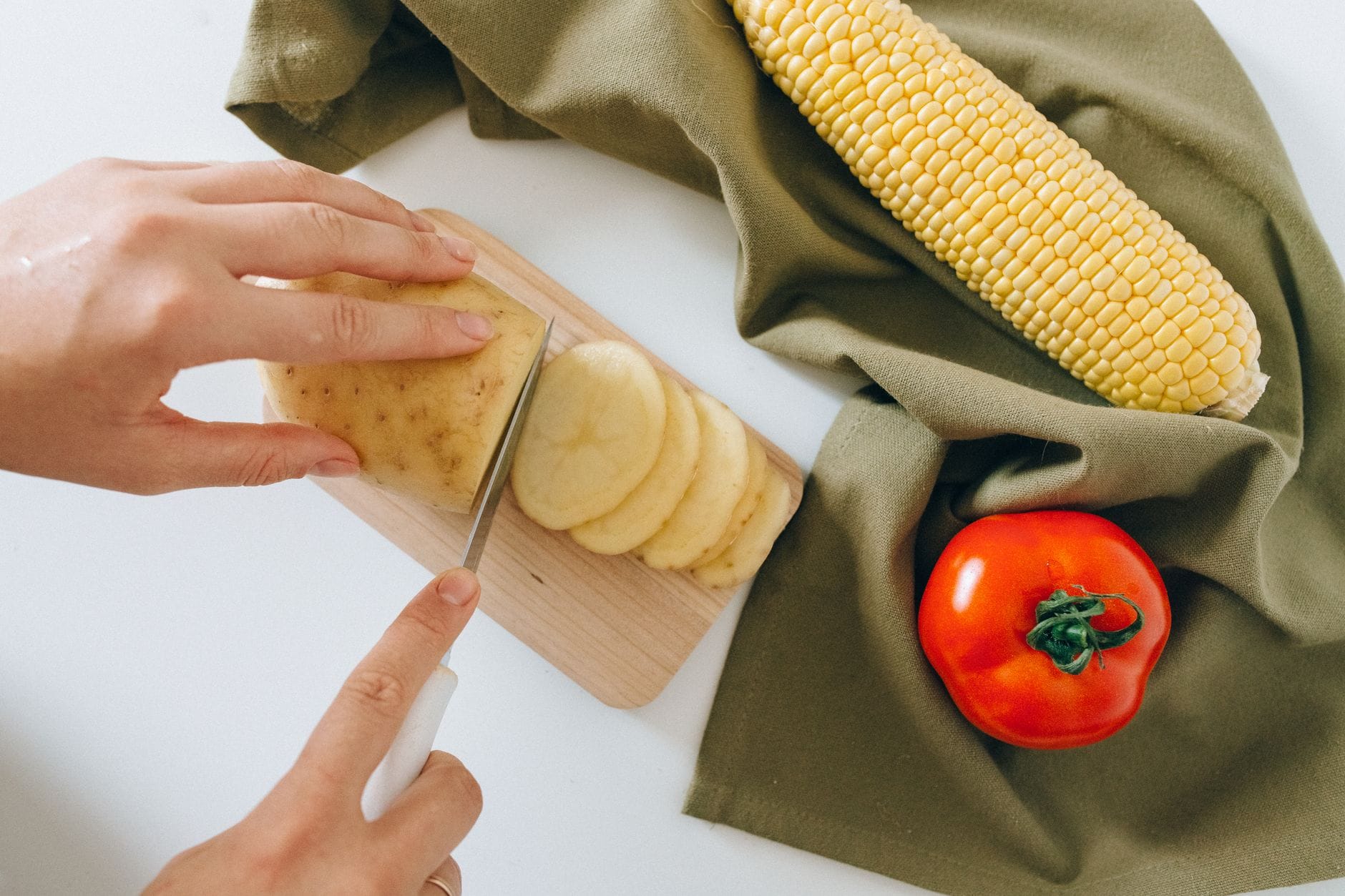 Hands slicing raw potatoes into cubes on a cutting board