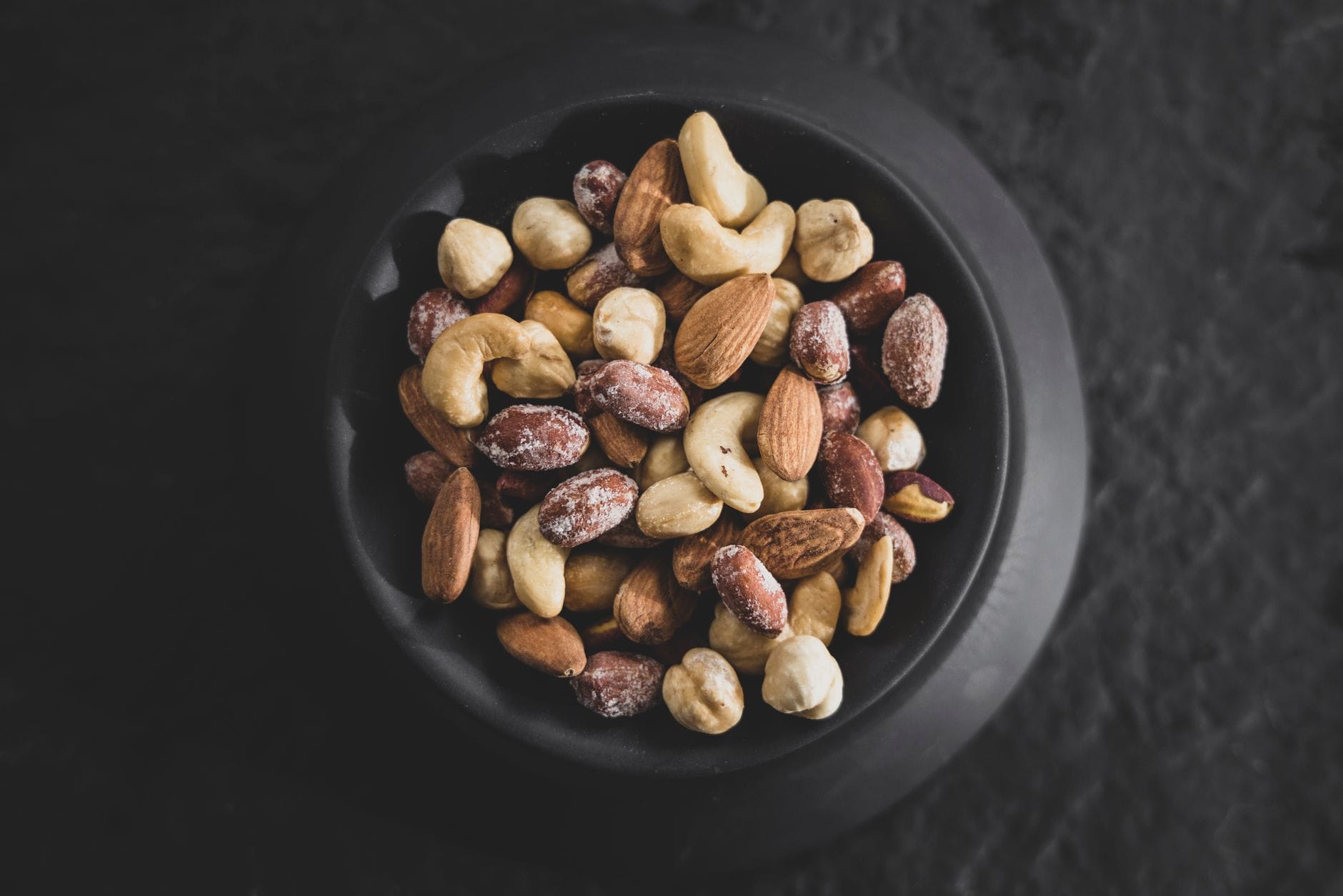 A wooden bowl filled with almonds walnuts and cashews on a table