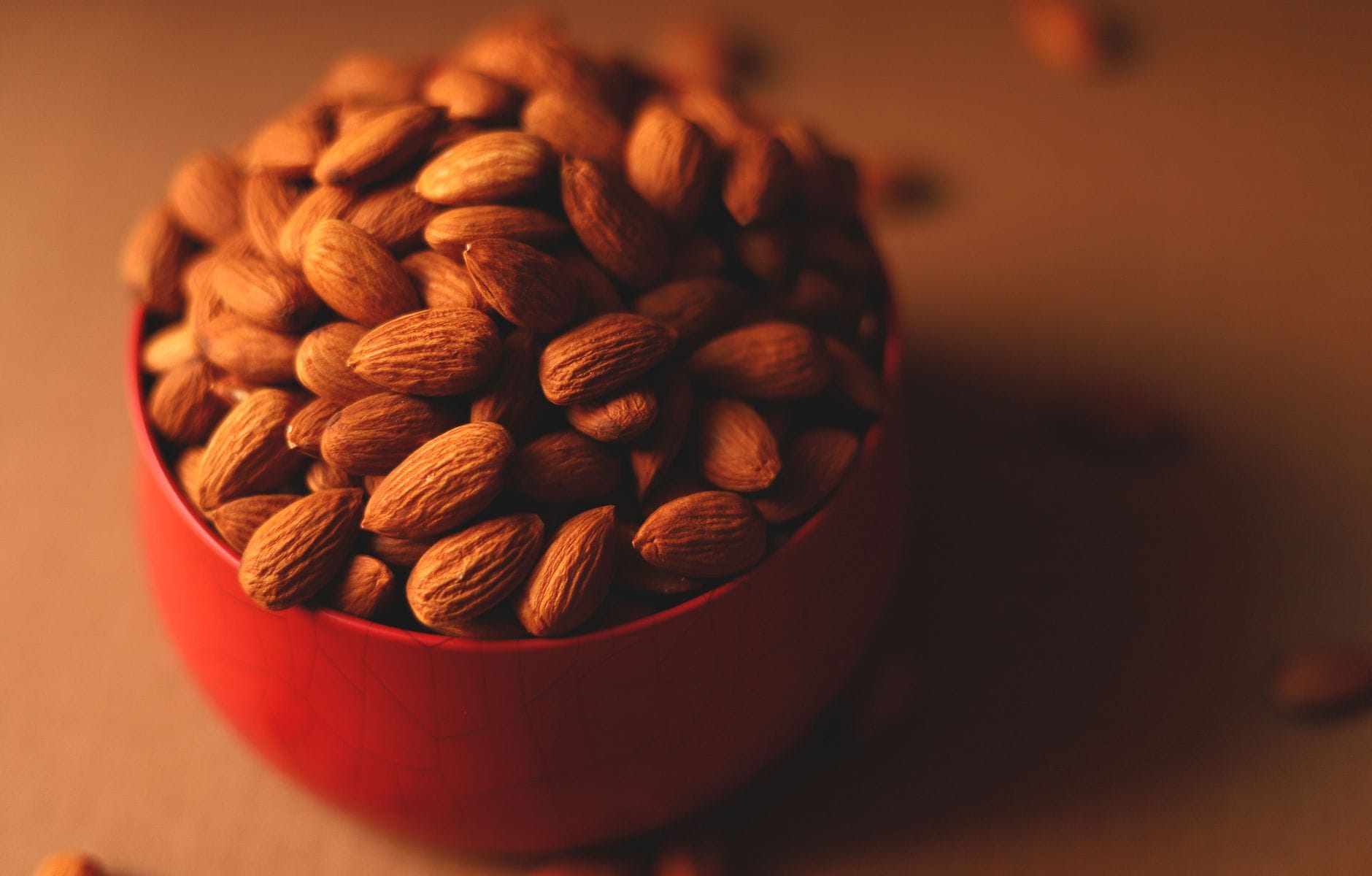 A small ceramic bowl filled with raw almonds on a wooden table