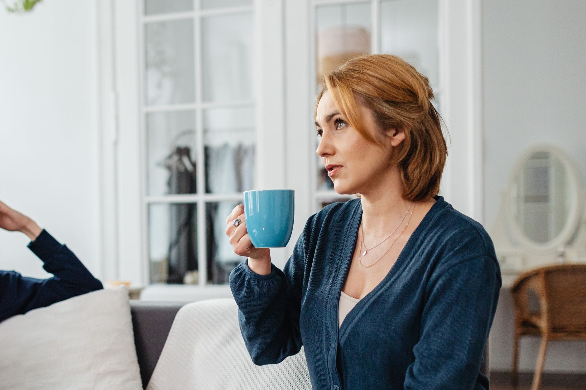 Woman in a cozy sweater curled up on a couch holding a warm mug