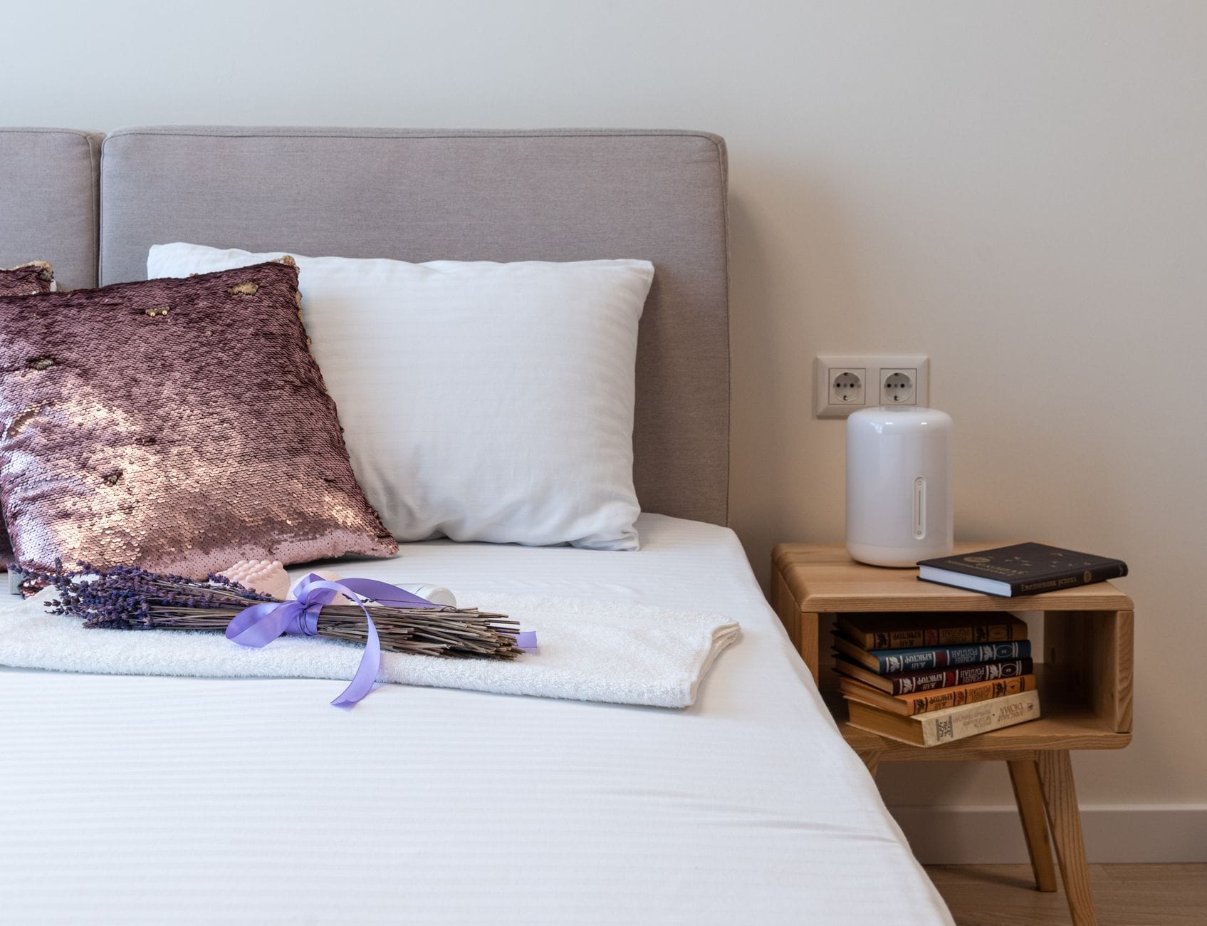 White cool-mist humidifier releasing vapor on a nightstand beside a bed