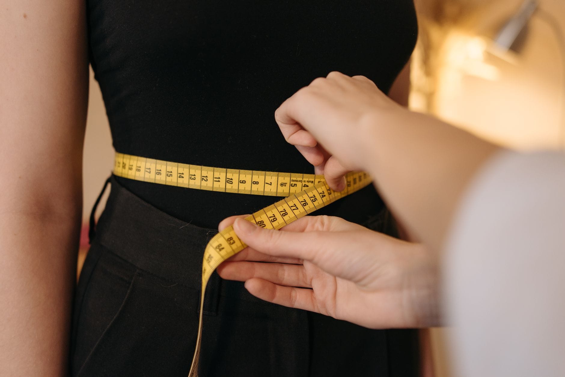 Yellow measuring tape wrapped around a person's waist against a plain background