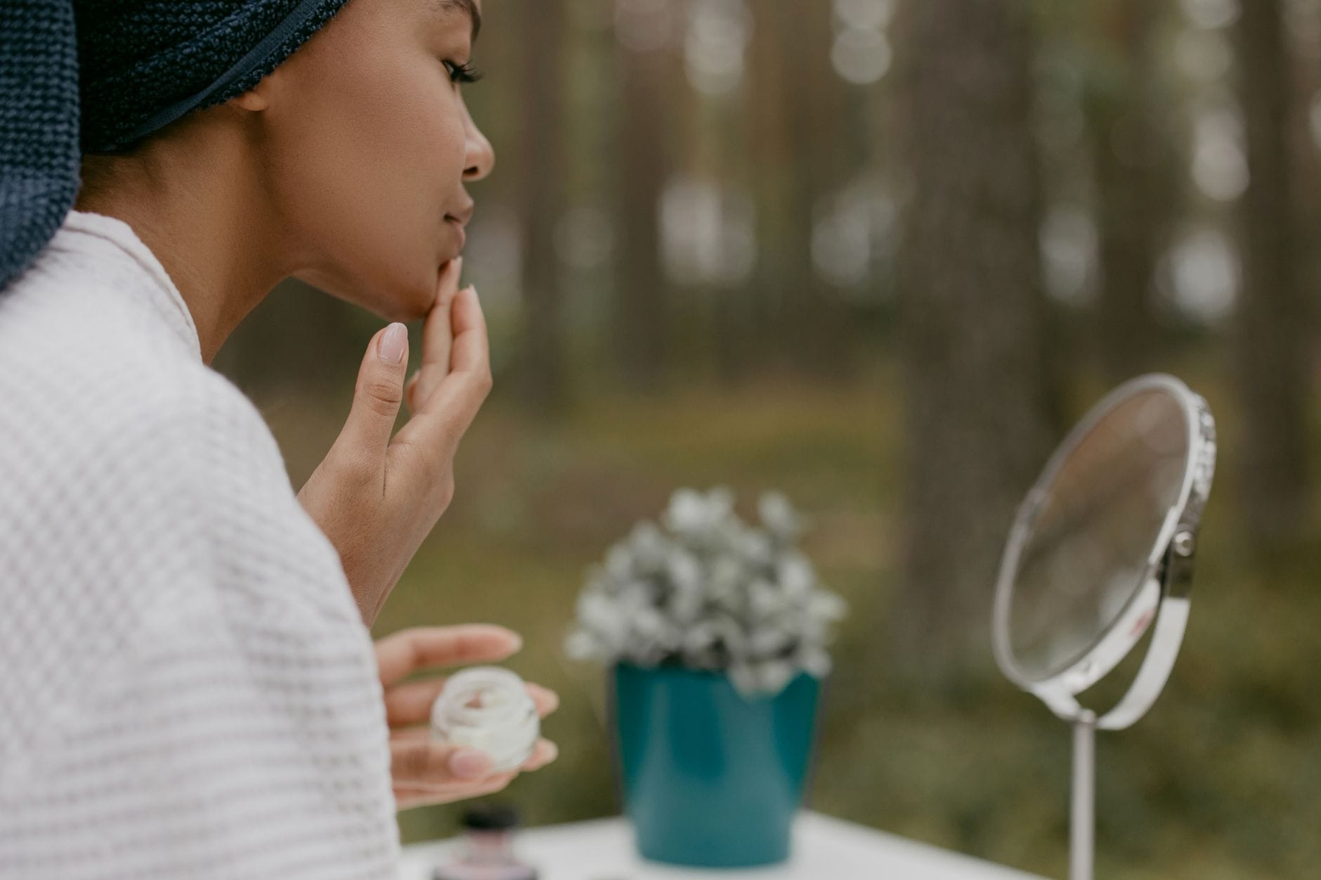 Close-up of a woman smoothing moisturizer onto her cheek by a mirror