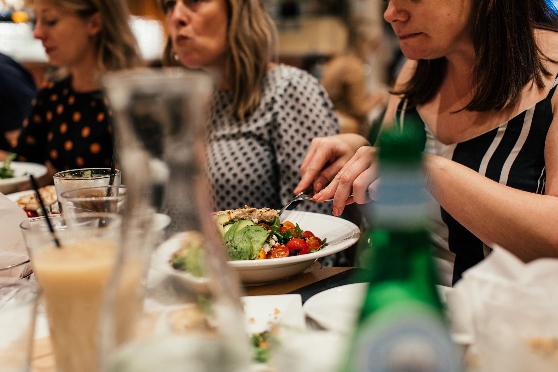 A young woman smiling while eating a fresh green salad at a table