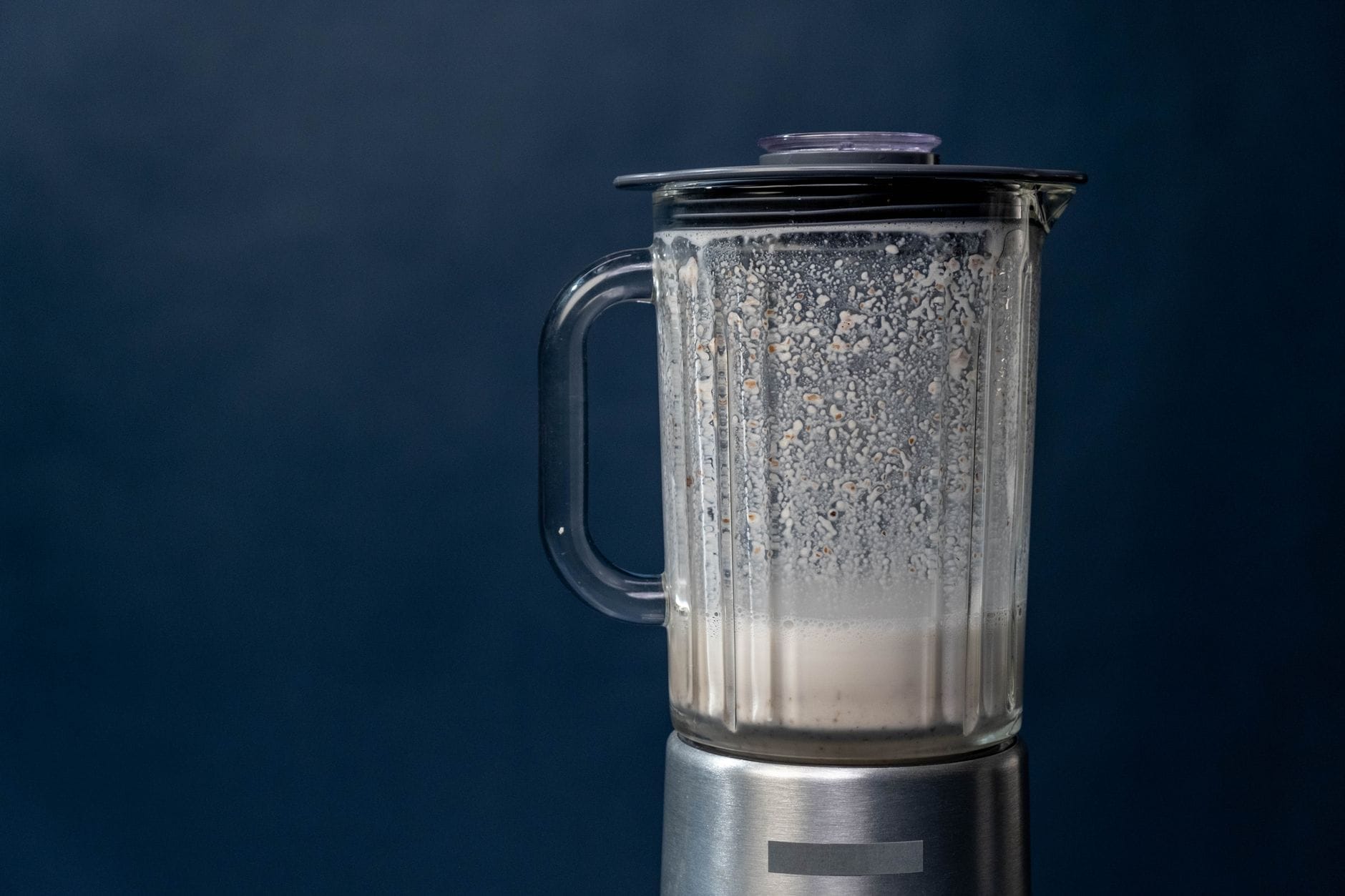 A blender pouring a creamy vanilla shake into a tall glass