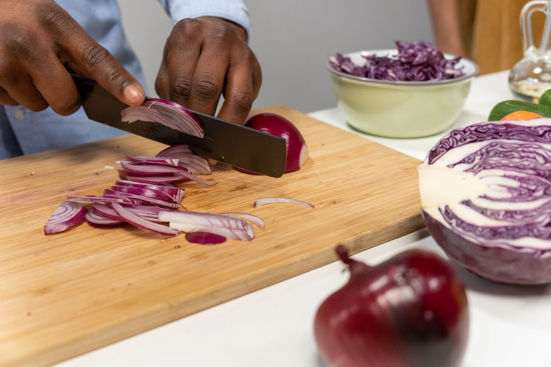 Hands slicing fresh vegetables on a wooden cutting board near a knife