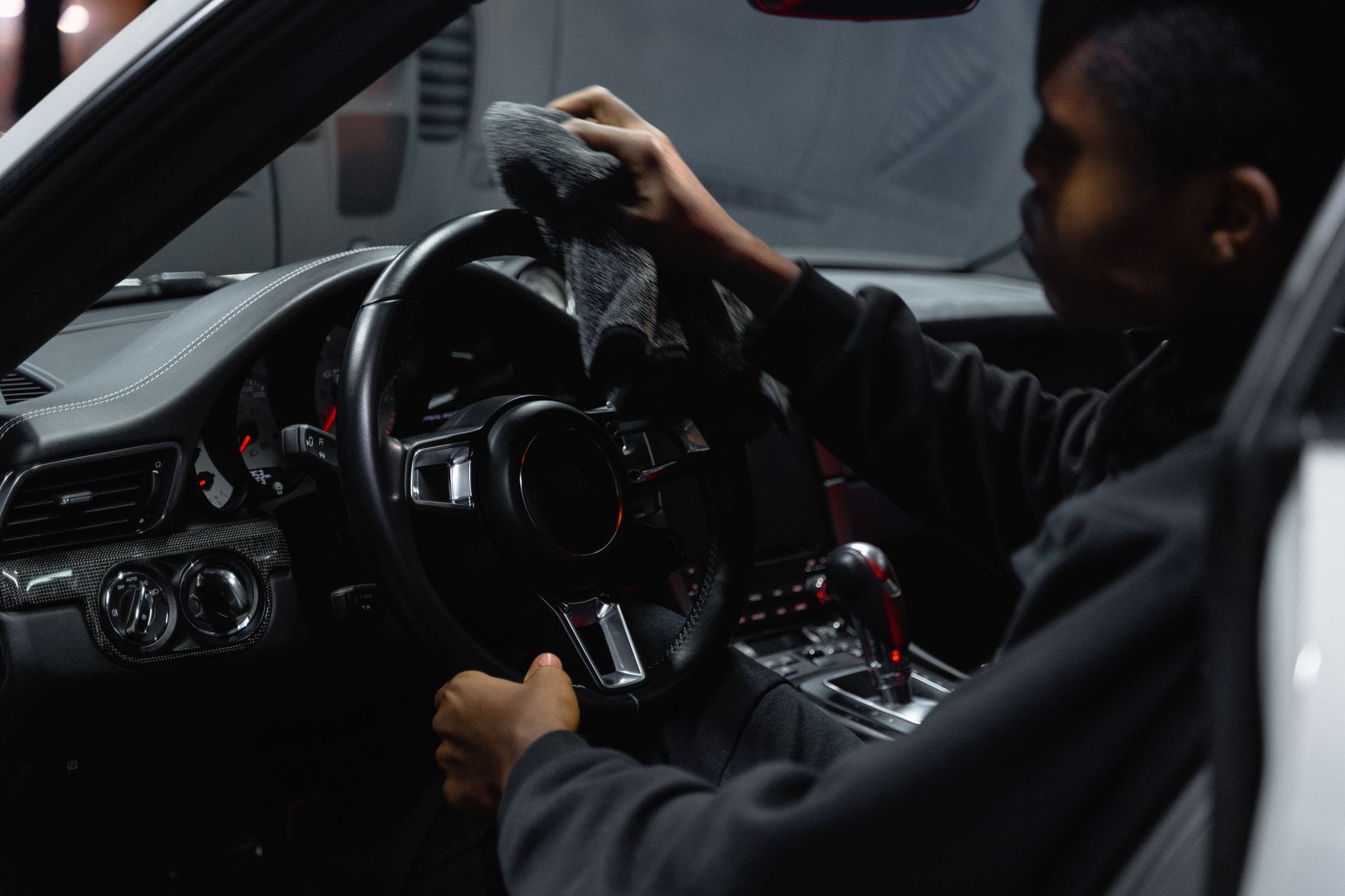 Gloved hand wiping down a car seat with a cloth inside a vehicle