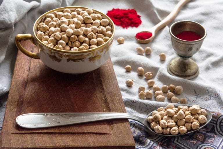 Pile of dried beige chickpeas spilling from a rustic ceramic bowl