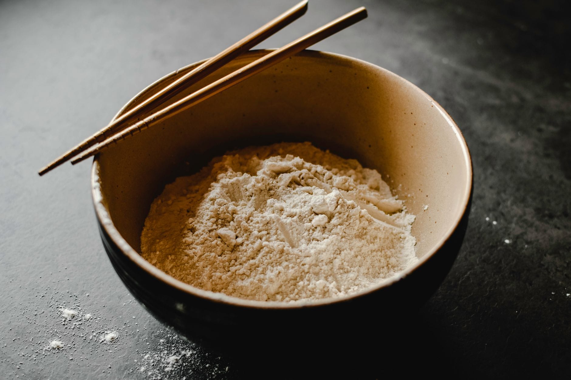 White coconut flour in a ceramic bowl next to a halved brown coconut