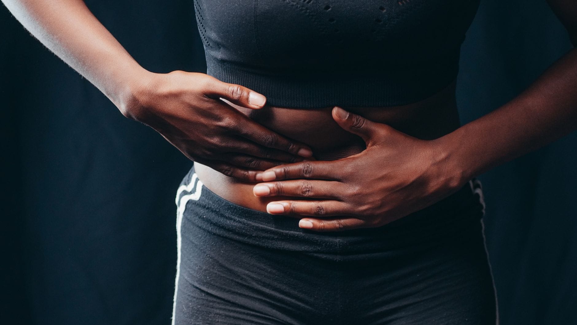 A woman on a couch holding her abdomen with a pained expression