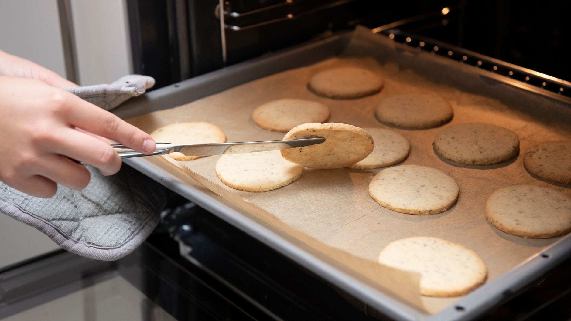 Freshly baked cookies cooling on a metal tray near an open oven
