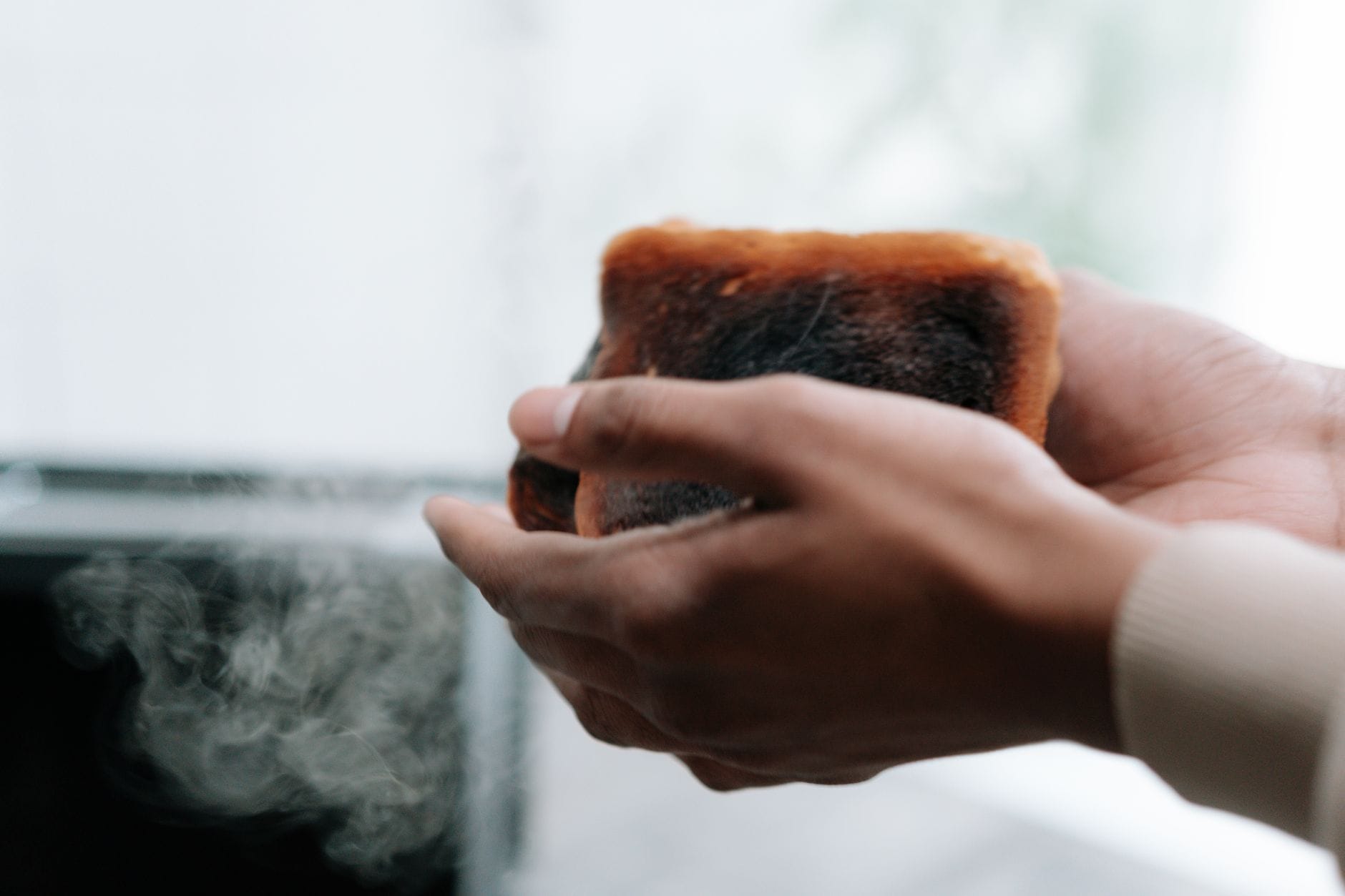 A hand holding a slice of golden toast beside a breakfast plate