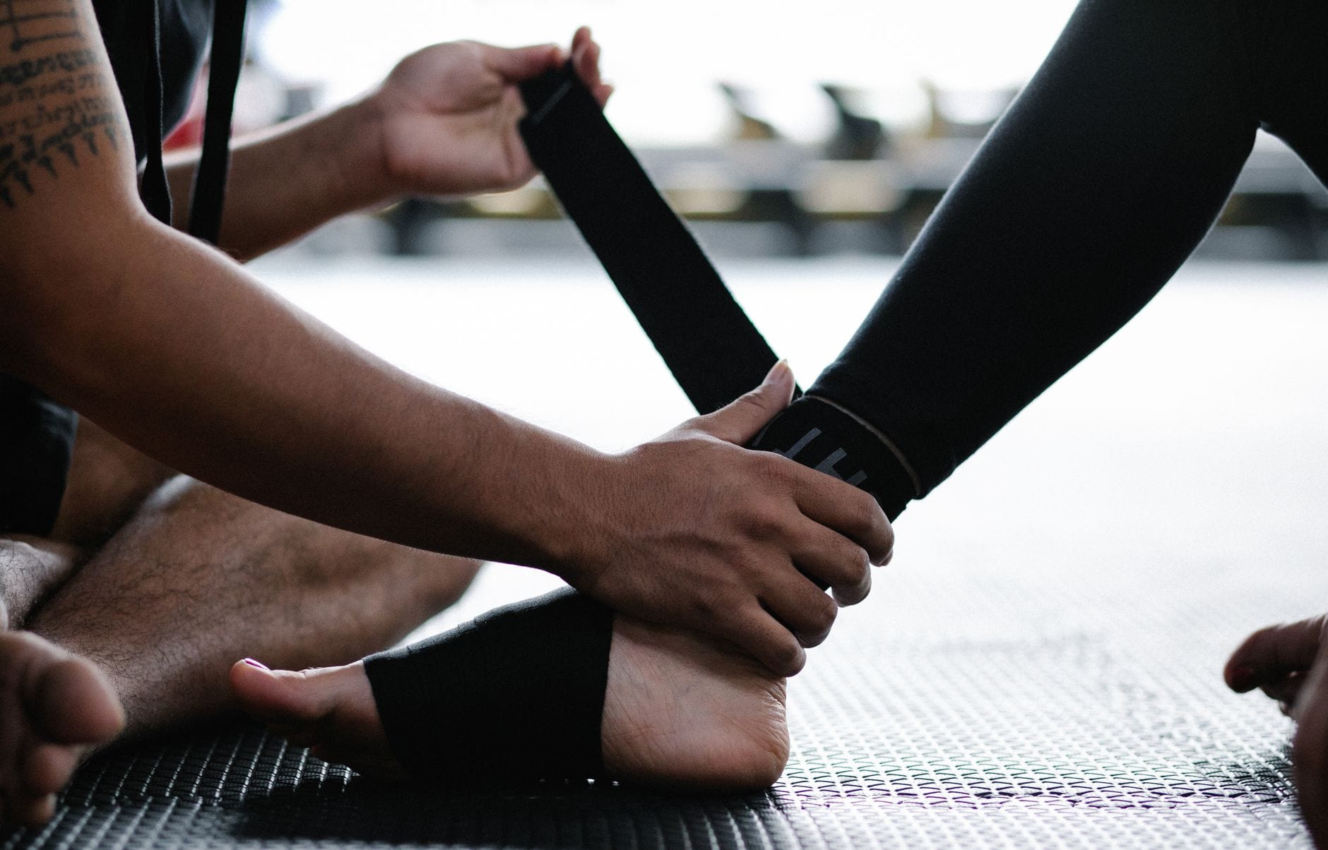 Hands wrapping a beige compression bandage around a bare foot and ankle