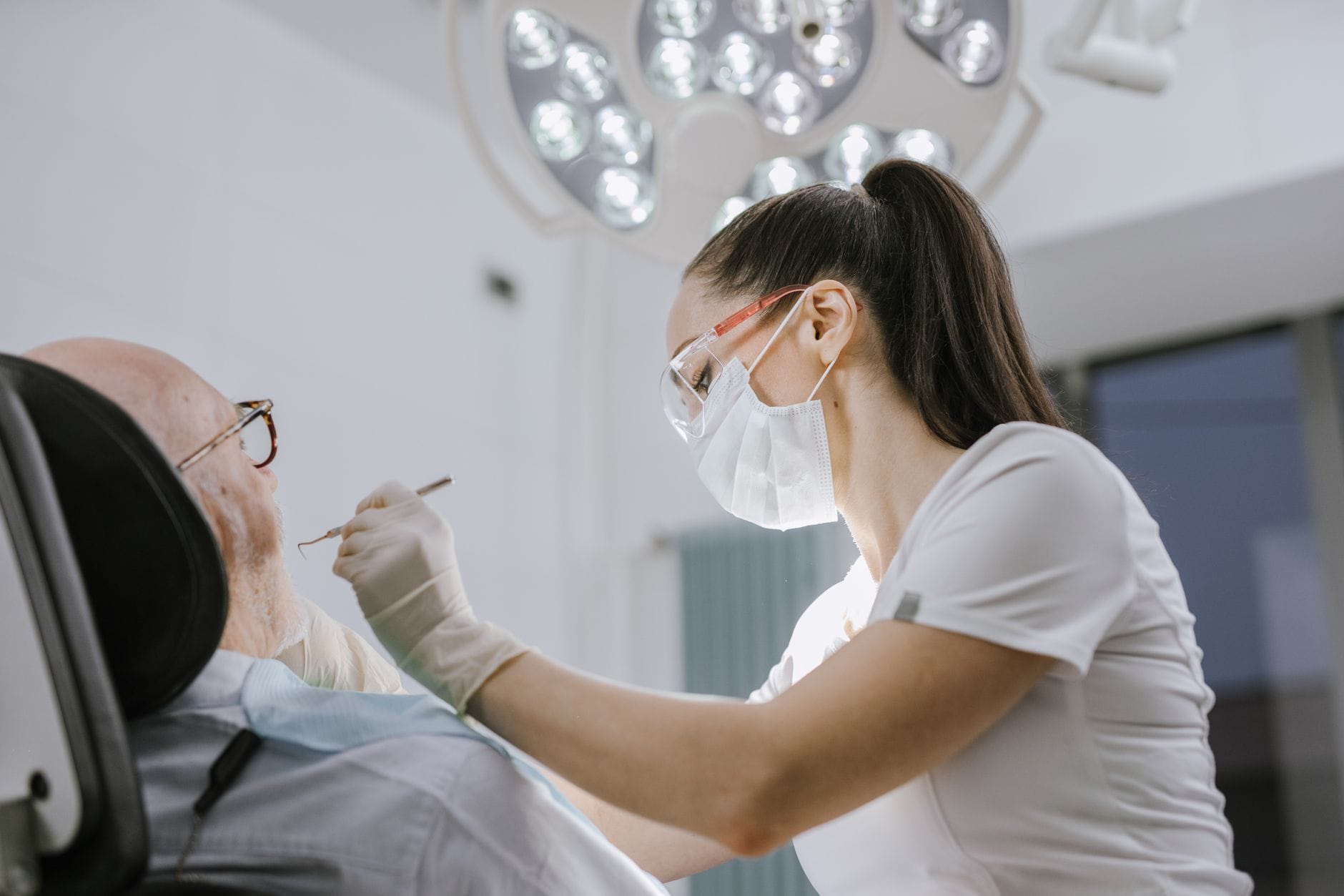 A dentist in gloves checking a patient's teeth with a mirror