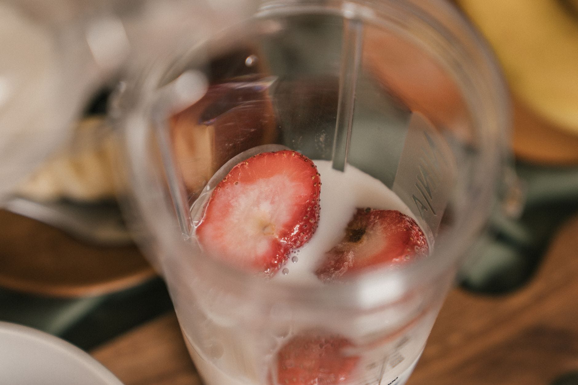 A blender filled with pink smoothie surrounded by fresh strawberries and bananas