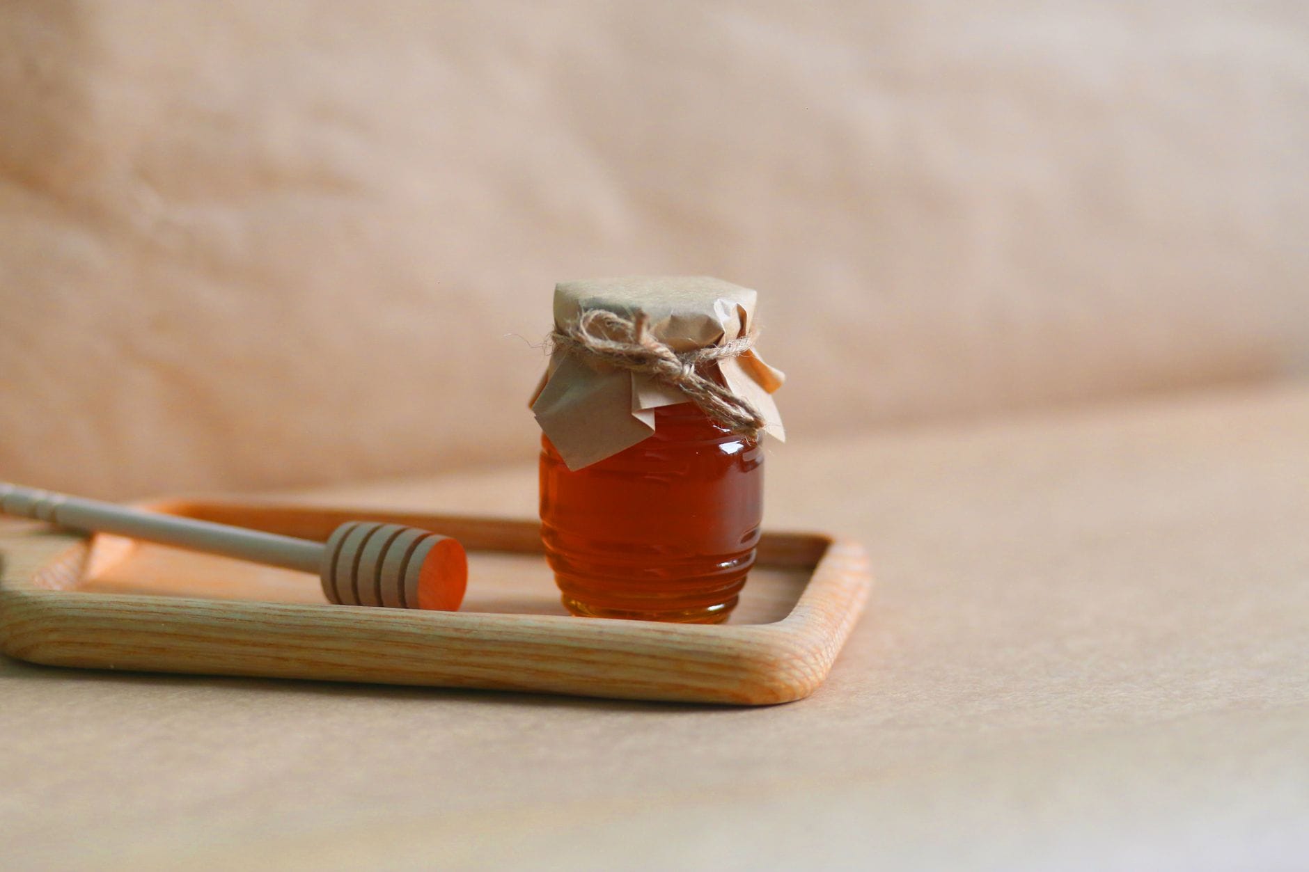An open jar of golden raw honey with a wooden dipper