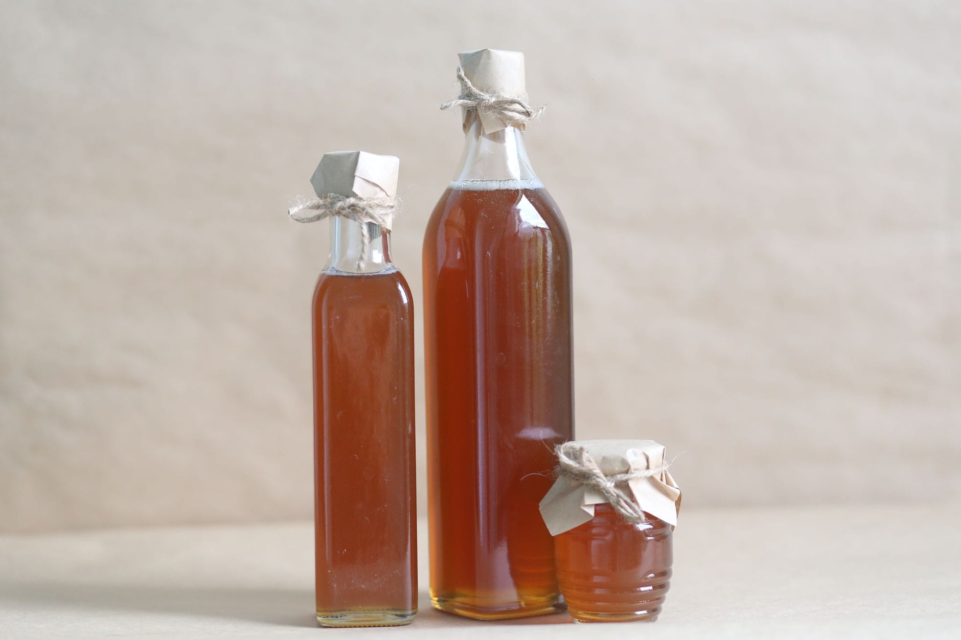 A glass bottle of amber maple syrup and a jar of golden honey side by side on wood