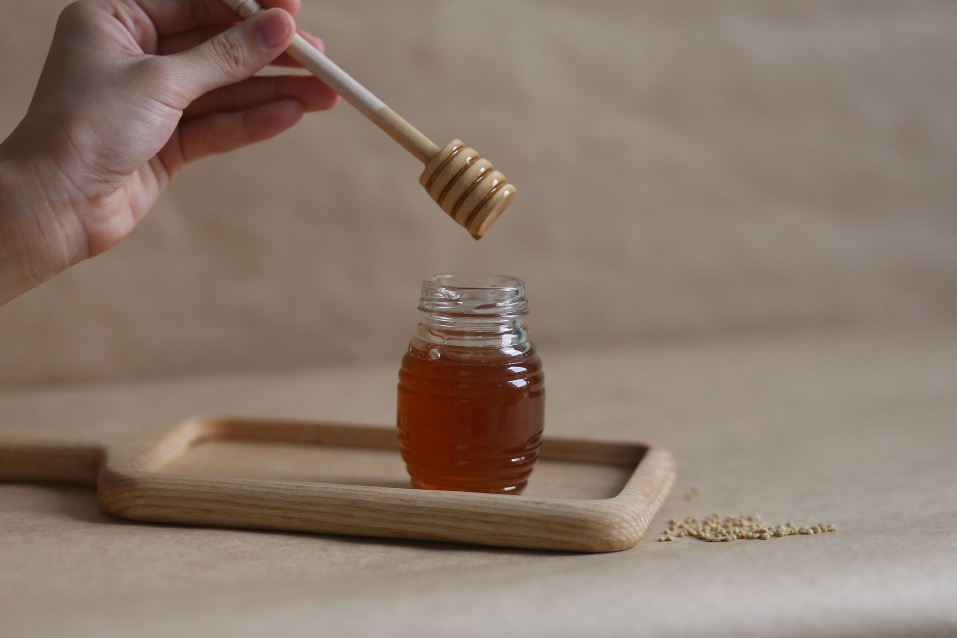 Golden honey dripping from a wooden dipper into a glass jar