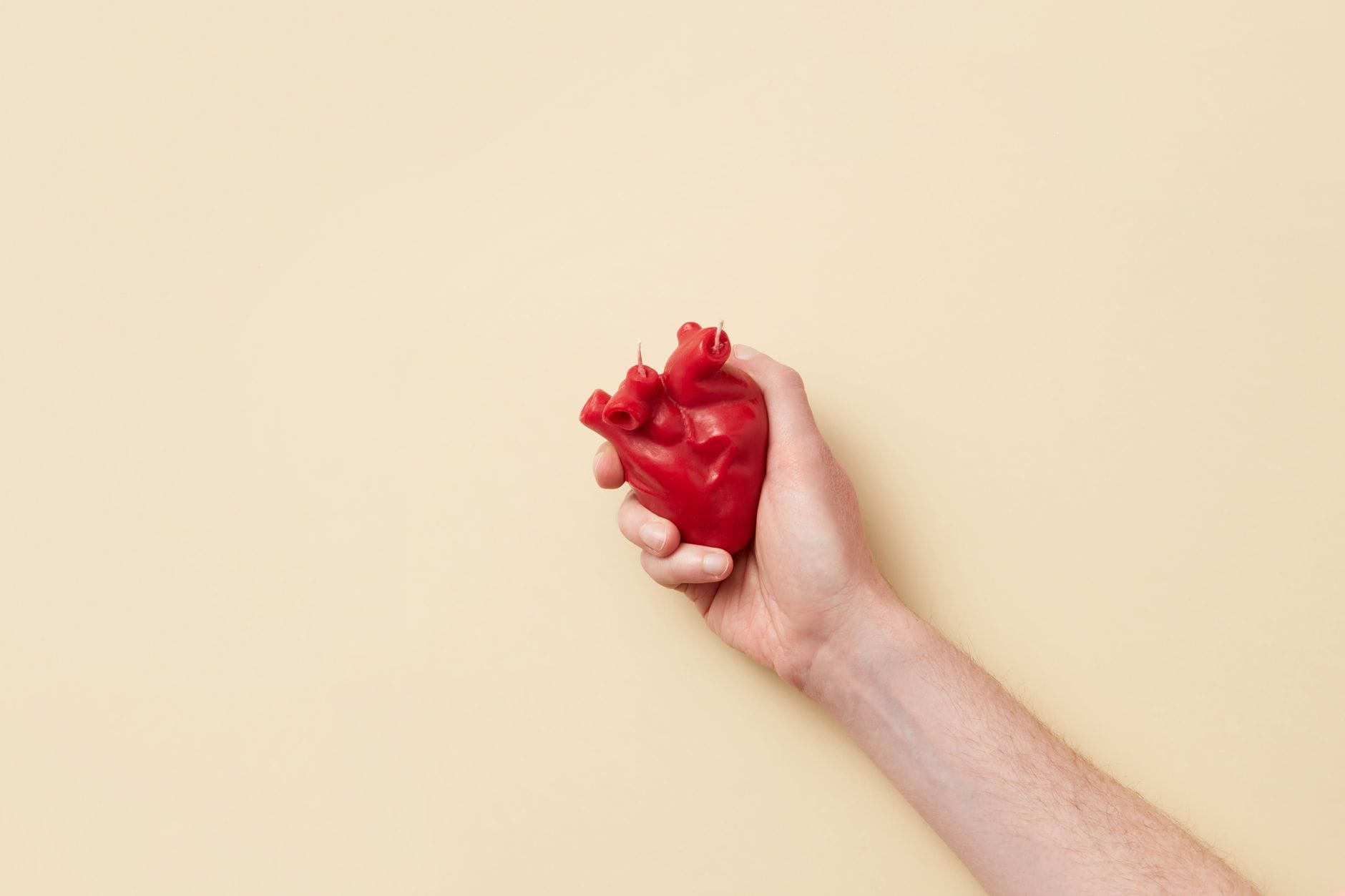 A red anatomical heart model resting on a light wooden surface