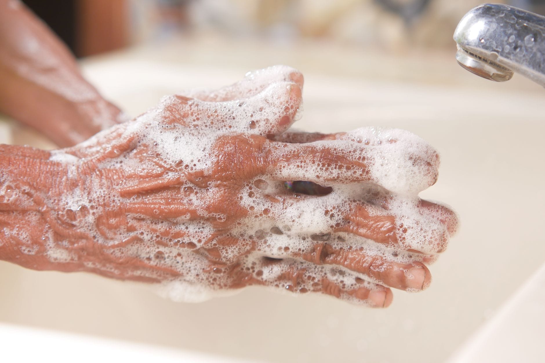 Soapy hands being scrubbed together under a running faucet