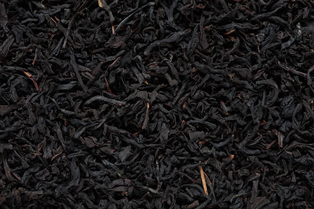 Dried green tea leaves spilling from a wooden scoop onto a table